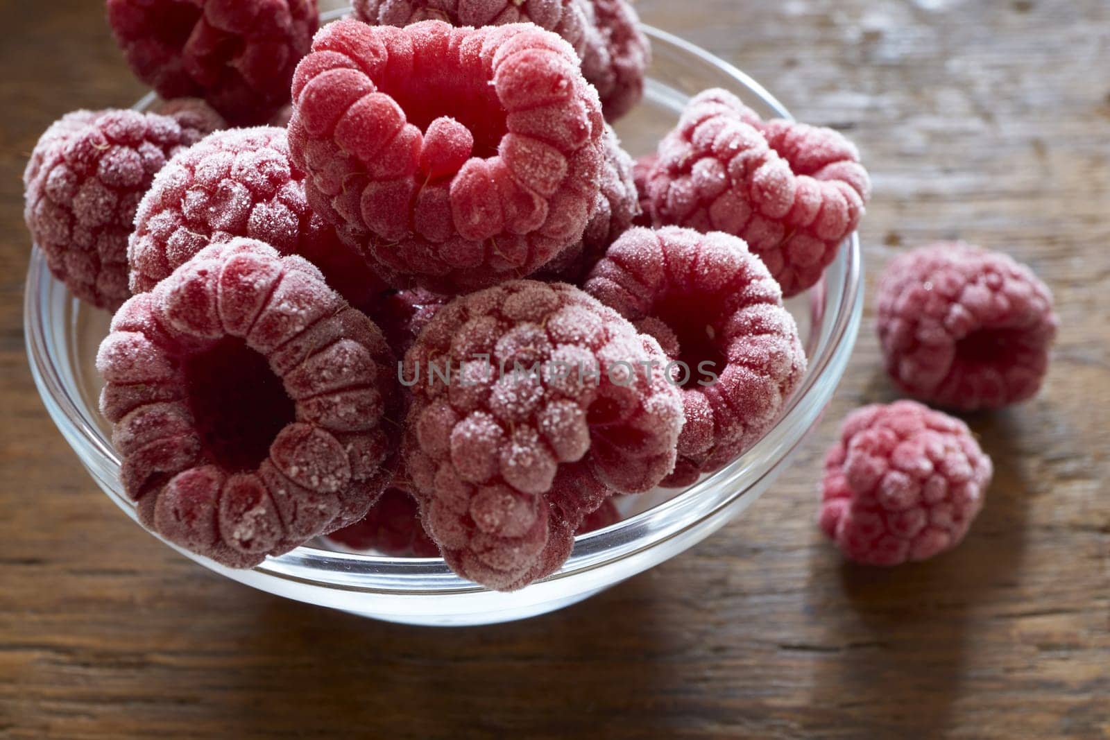 Frozen raspberries in a glass bowl on a wooden table