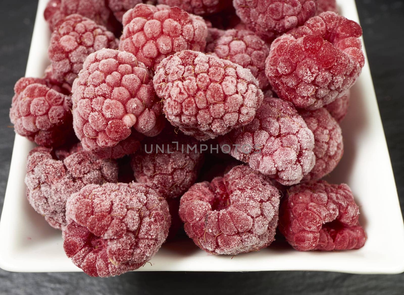 Frozen raspberries in porcelain bowl on slate plate