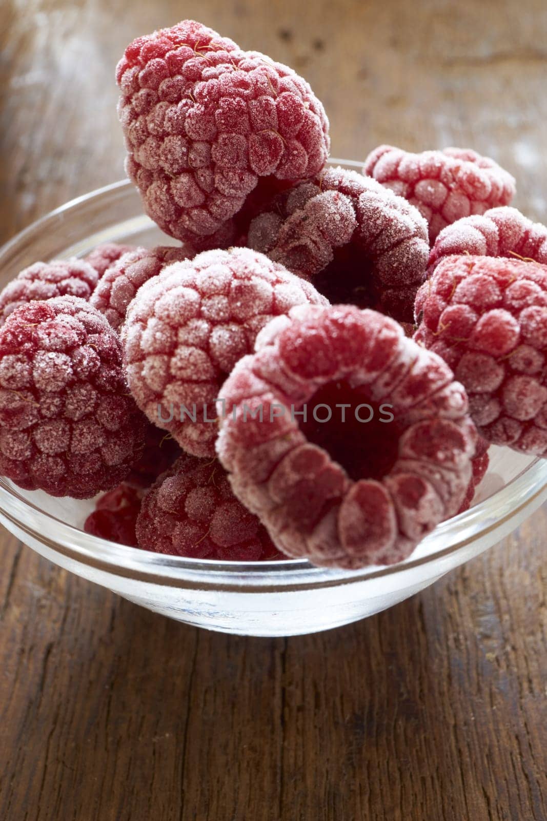 Frozen raspberries in a glass bowl on a wooden table