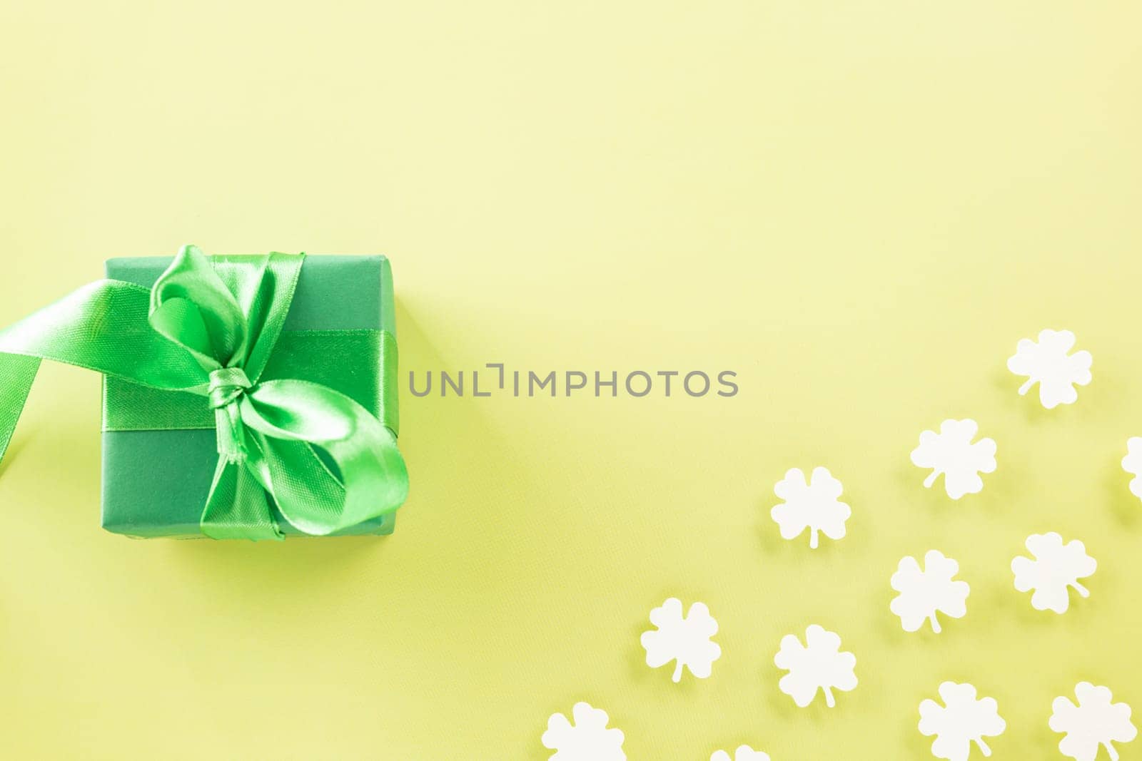 Happy St Patrick's Day decoration background concept. Top view gift box green clover leaves, shamrocks leaves holiday symbol with copy space on pastel yellow background