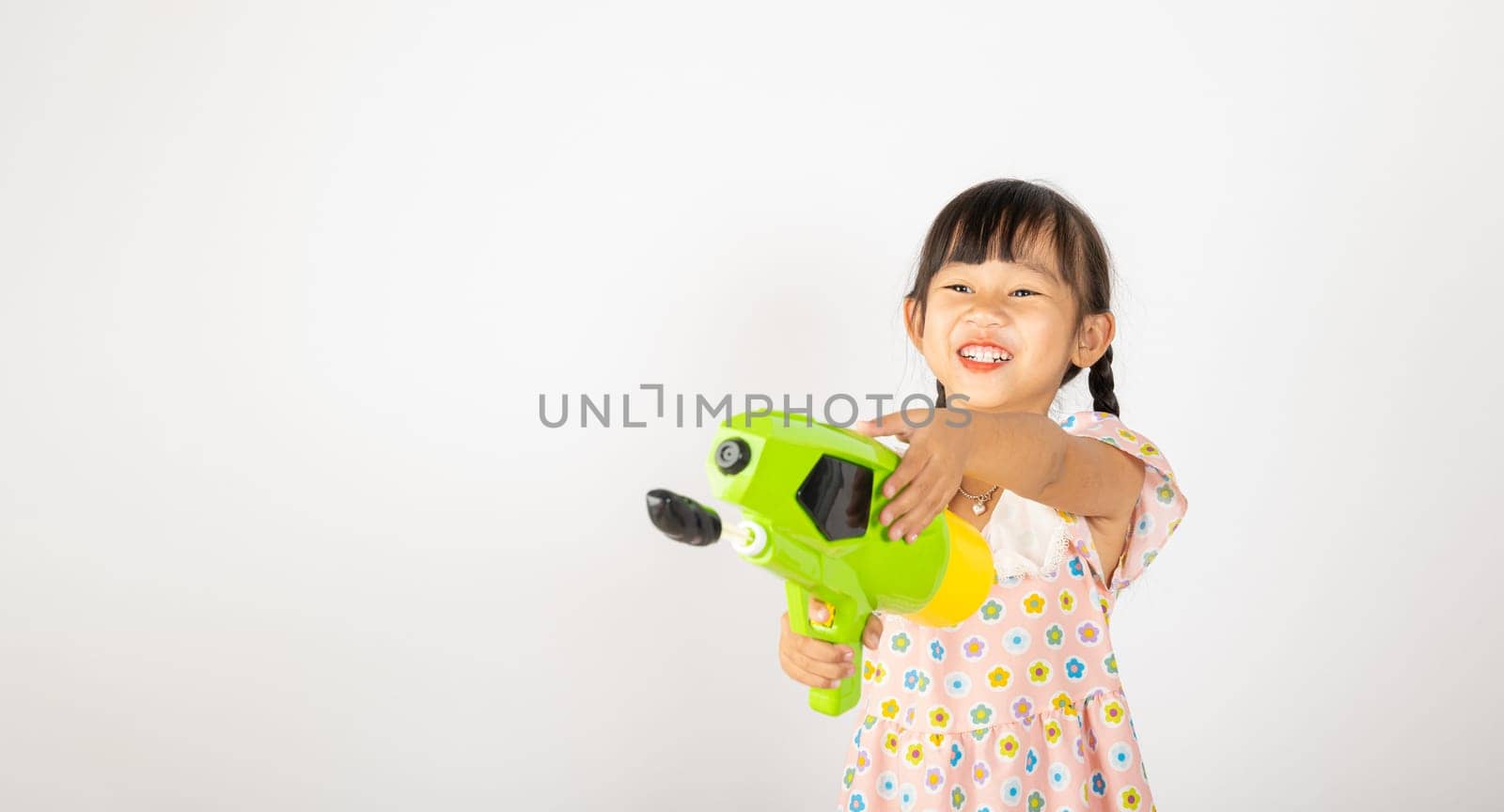 Happy Songkran Day, Asian little girl holding plastic water gun, Thai child funny hold toy water pistol and smile, isolated on white background, Thailand Songkran festival national culture concept