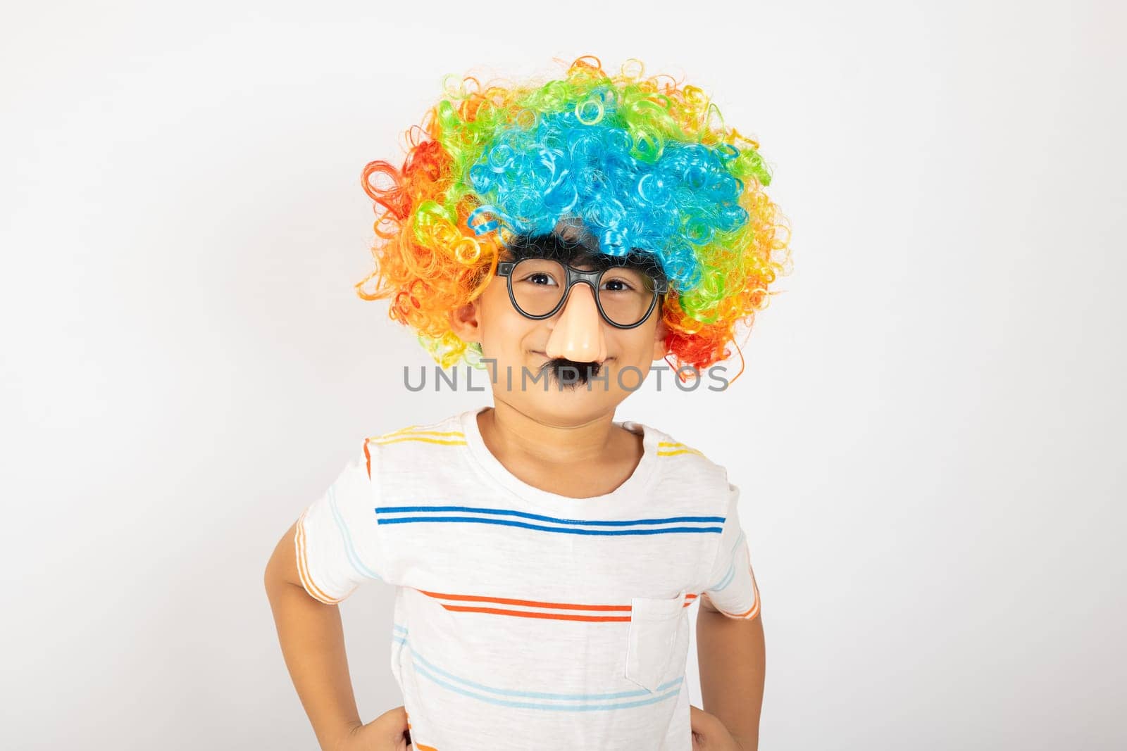 April Fool's Day. Portrait of Funny kid boy clown wears a curly wig colorful a big nos and glasses and has a mustache isolated on white background with copy space, Happy child festive decor