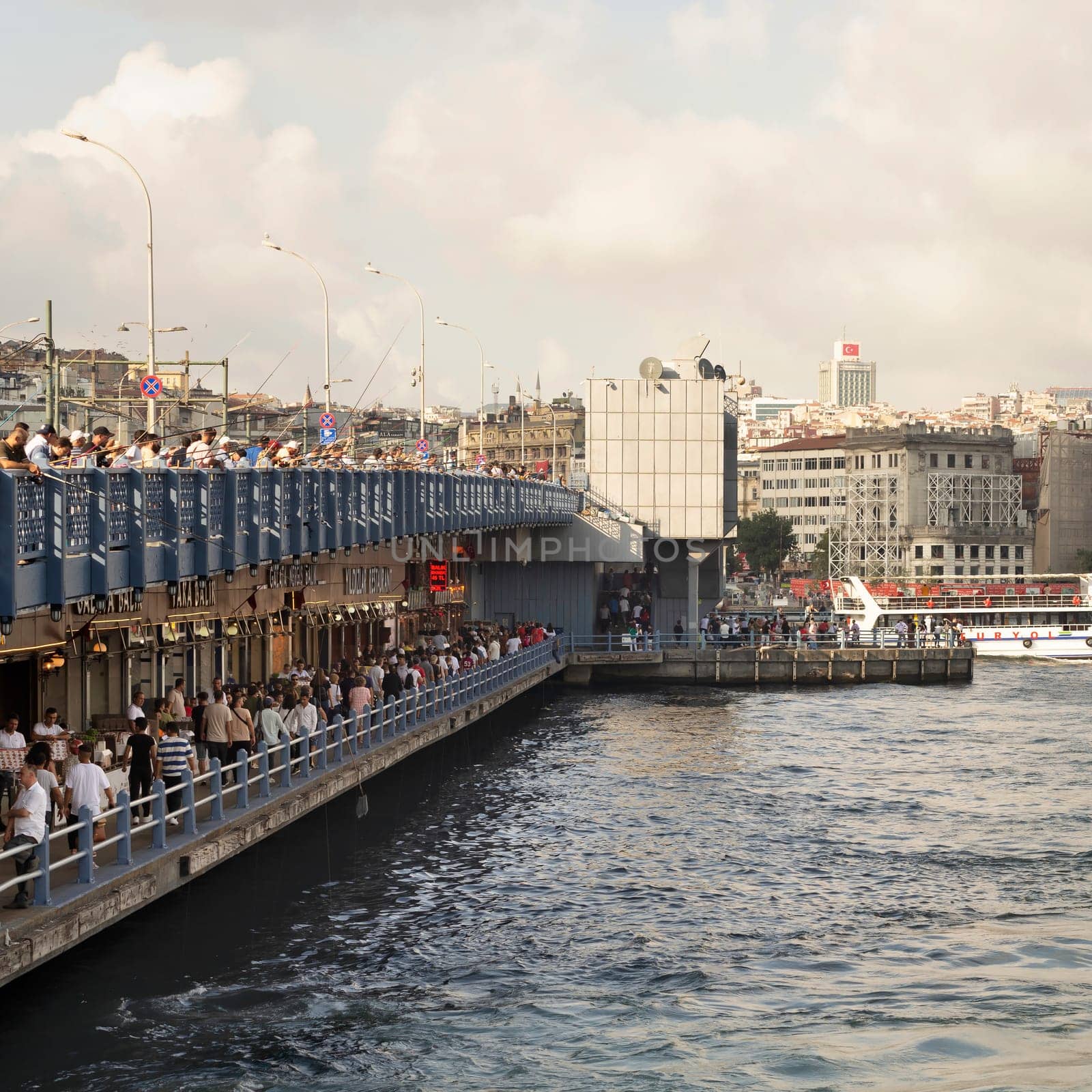 Istanbul, Turkey - August 30, 2022: Galata Bridge with traditional fish restaurants in the passage under the bridge, and crowds of People during Victory Day holiday