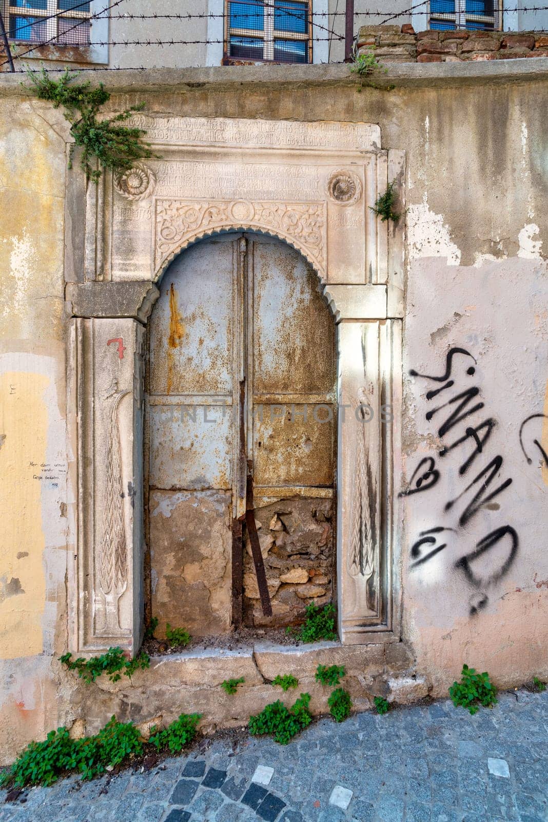 Exterior shot of grungy abandoned entrance with rusted metal door, in a cobblestone narrow street, Balat District, Istanbul, Turkiye