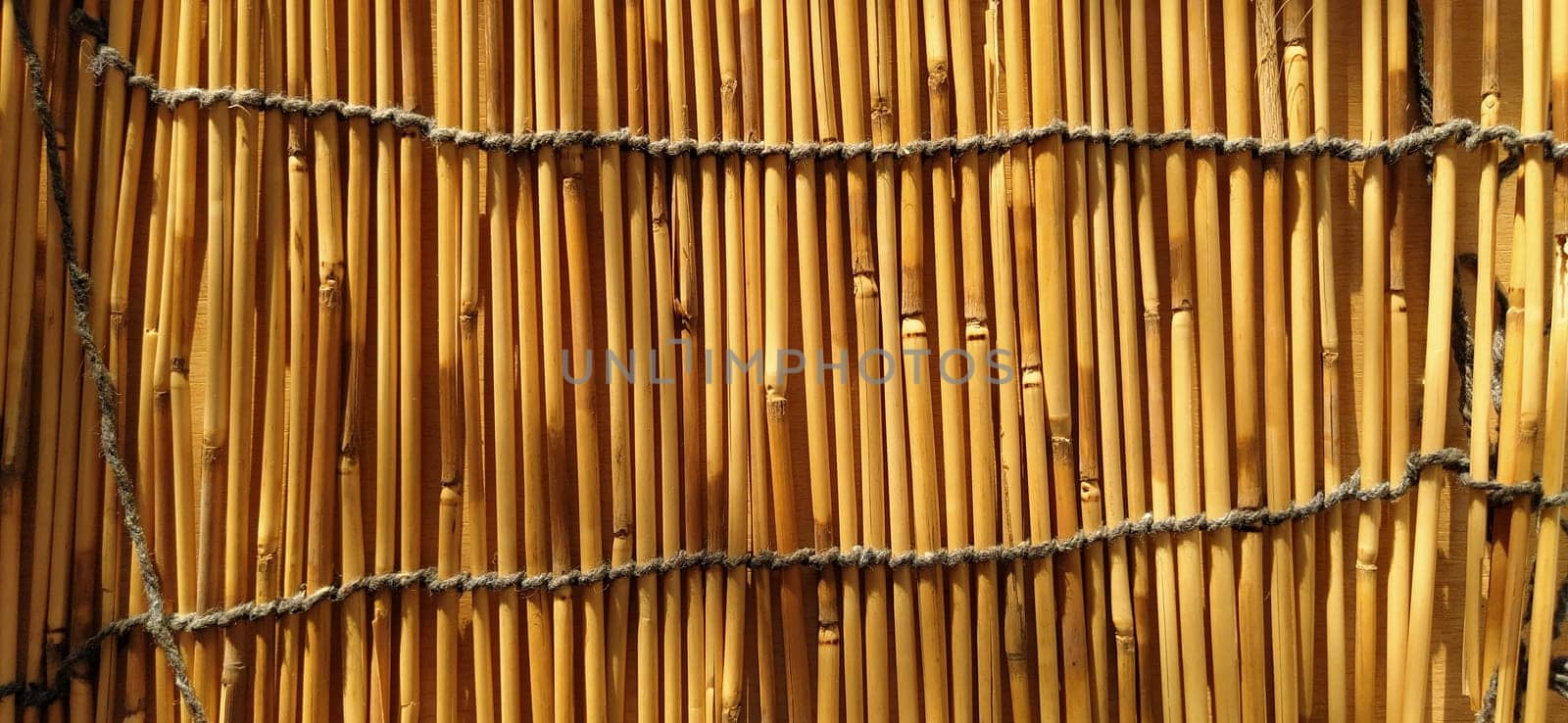A straw bedding, tablecloth or small rug laid on a table and photographed from the side. Soft evening sunlight reflects off the stems. Some sticks are broken, threads and ropes are braided.