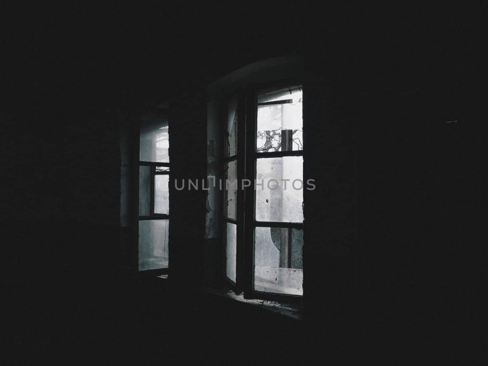 Scary windows. Inside an abandoned house. View of broken windows without a curtain. Grunge scene. Light shines through old wooden frames with broken glass. The concept of abandonment and uselessness.