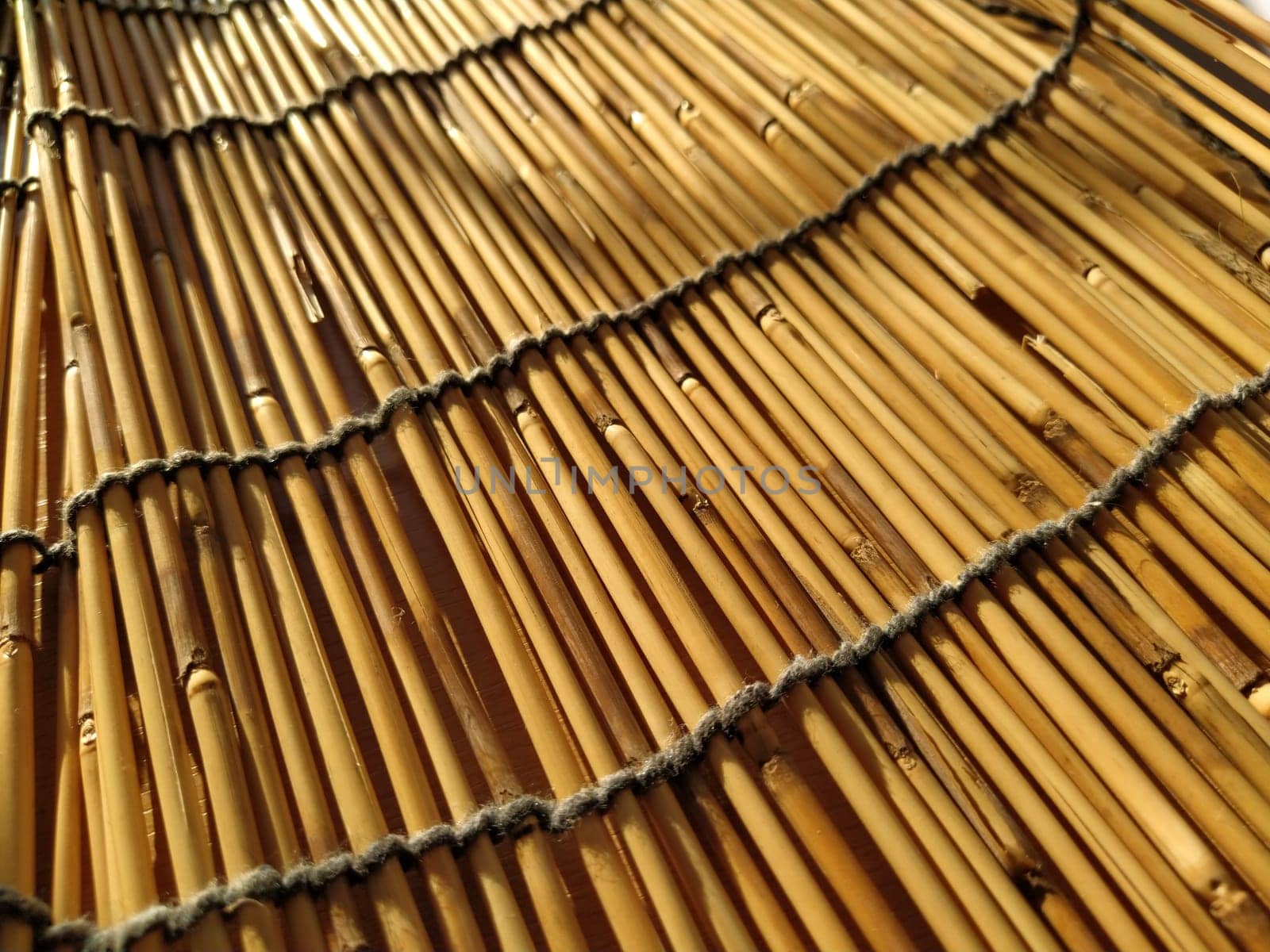 A straw bedding, tablecloth or small rug laid on a table and photographed from the side. Soft evening sunlight reflects off the stems. Some sticks are broken, threads and ropes are braided.