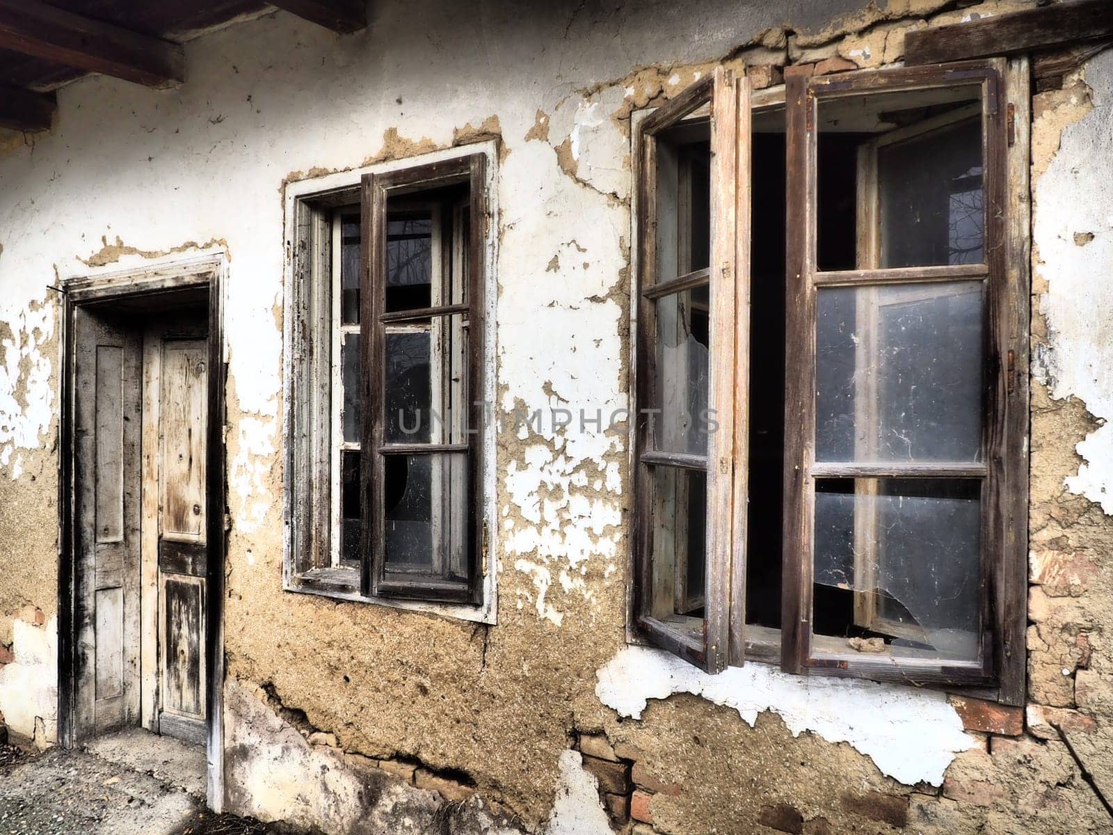 Old house with windows and a door. Collapsing rural house. The concept of urbanization and oblivion of the motherland. Abandoned house. Broken glass in the window and falling plaster. Serbia. Balkans.