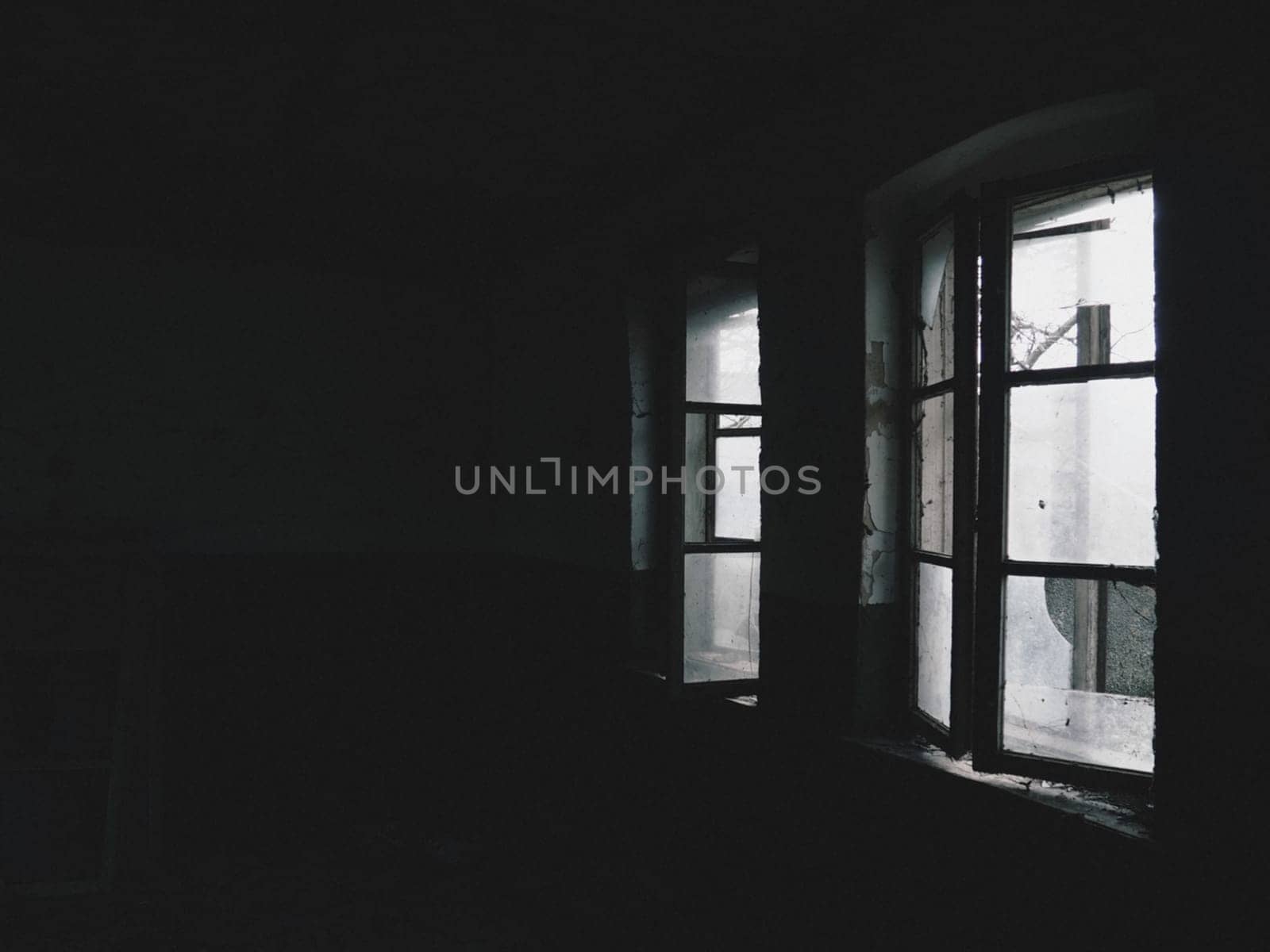 Scary windows. Inside an abandoned house. View of broken windows without a curtain. Grunge scene. Light shines through old wooden frames with broken glass. The concept of abandonment and uselessness.