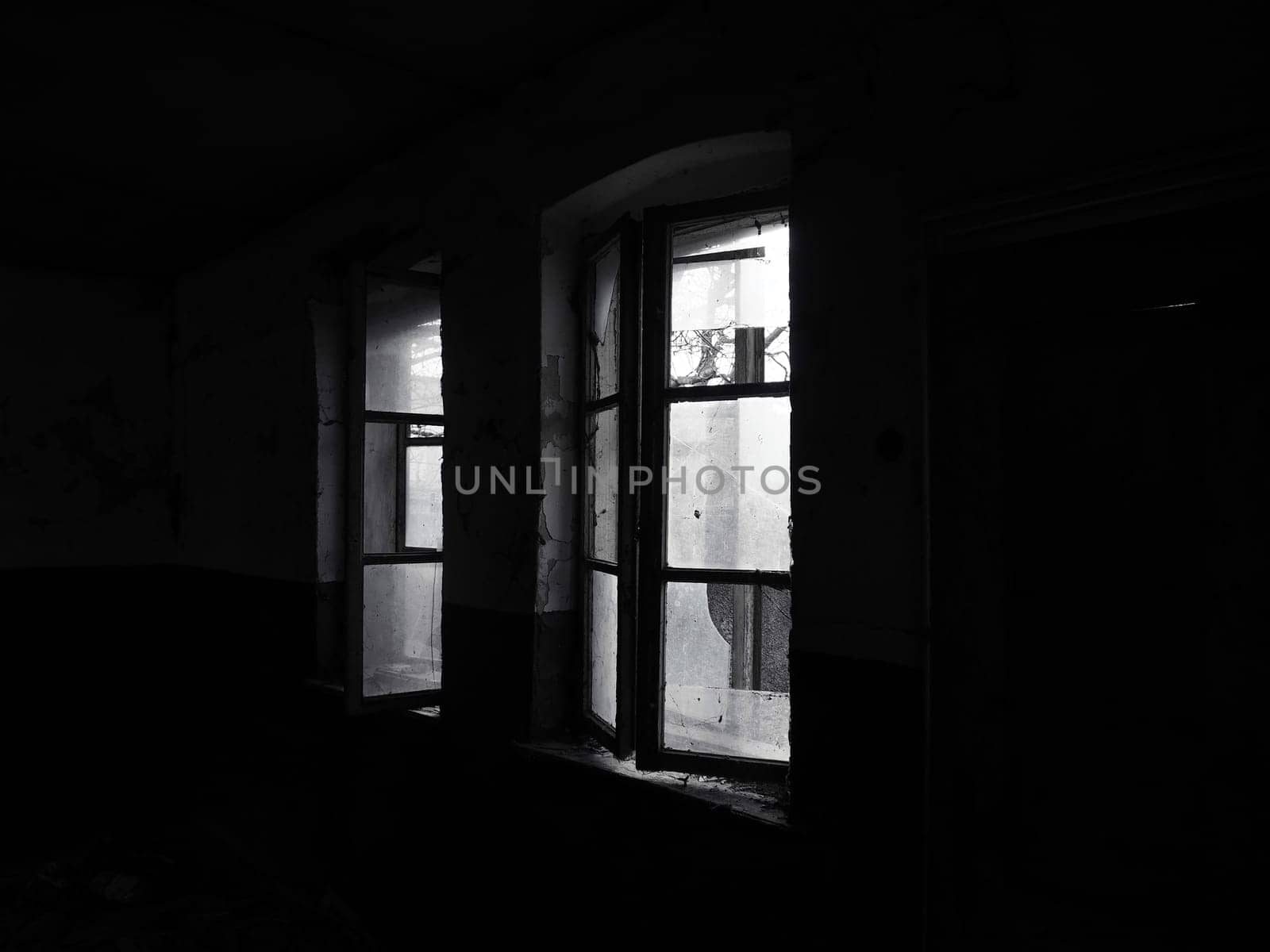 Scary windows. Inside an abandoned house. View of broken windows without a curtain. Grunge scene. Light shines through old wooden frames with broken glass. The concept of abandonment and uselessness.