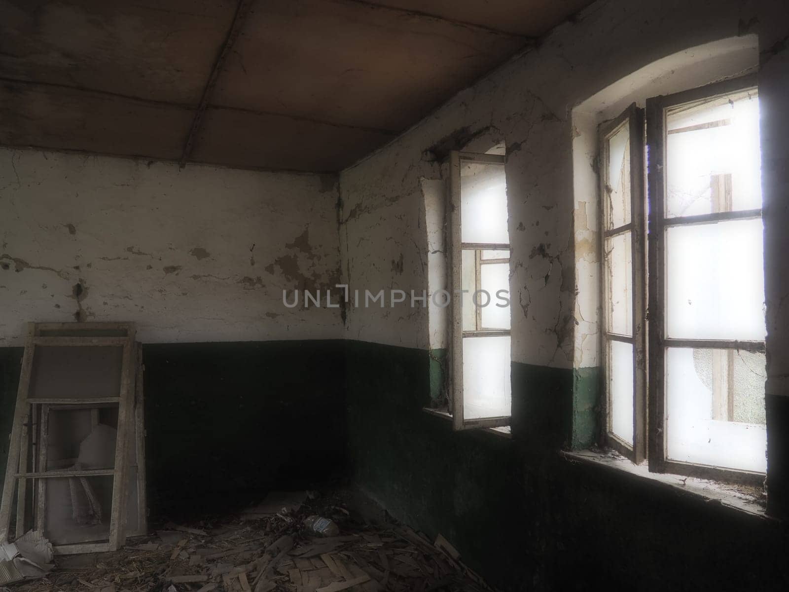 Scary windows. Inside an abandoned house. View of broken windows without a curtain. Grunge scene. Light shines through old wooden frames with broken glass. The concept of abandonment and uselessness.