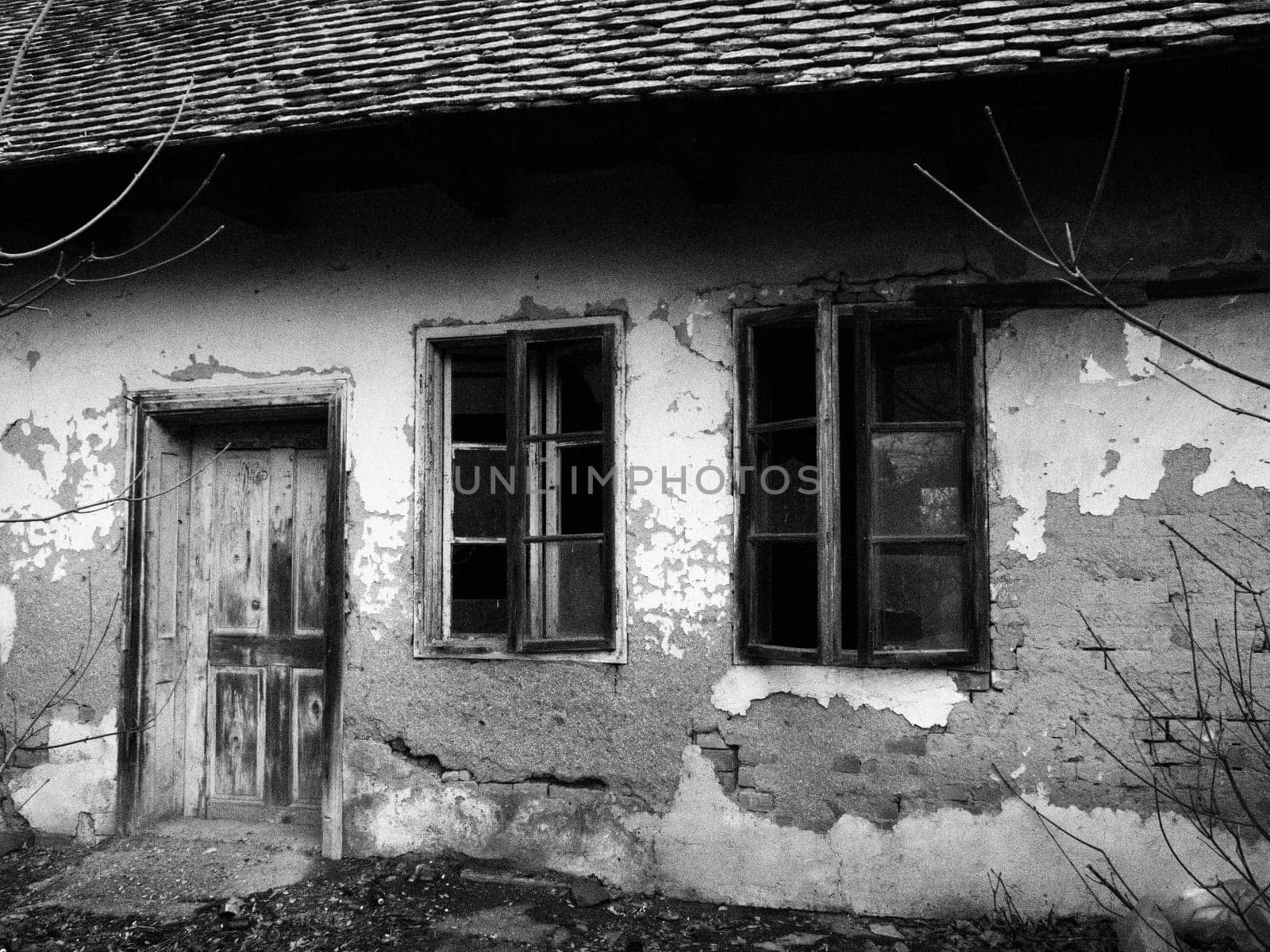 Old house with windows and a door. Collapsing rural house. The concept of urbanization and oblivion of the motherland. Abandoned house. Broken glass in the window and falling plaster. Serbia. Balkans.