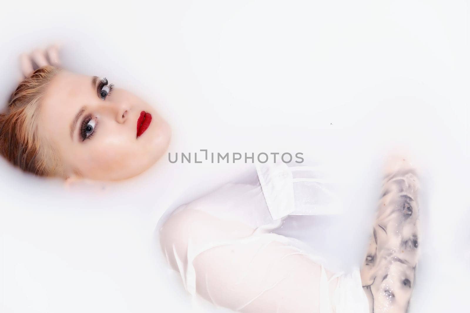 Girl with red lips and  tattoo on her hand is lying  in spa bath with milk. Horizontally.