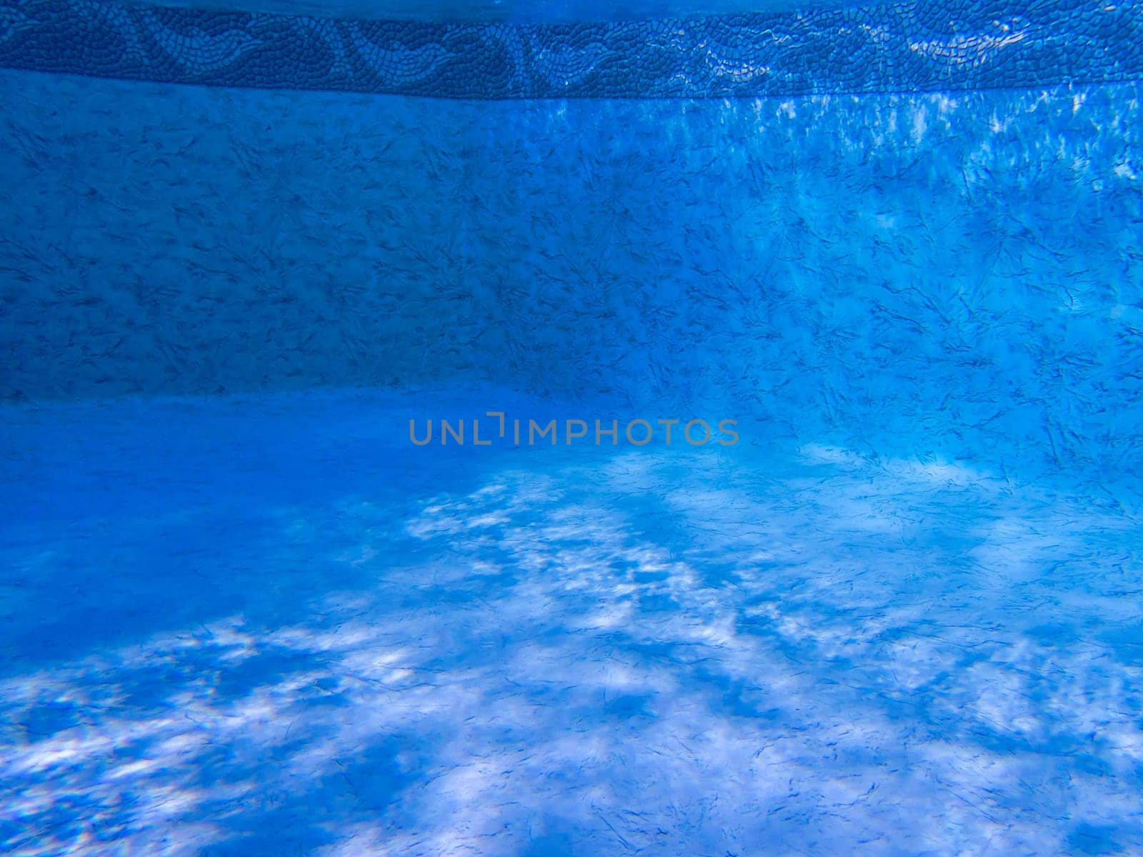 Dreamy clean blue pool interior shot underwater with dolphin boeder and ripples of light and shadow.