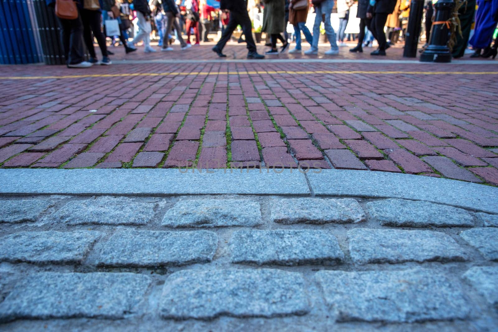 Cobblestone and brick historic street closeup with pedestrian feet crossiing in background with yellow Freedom Trail line visible on bricks. Sunny outdoor day in Boston with copy space.