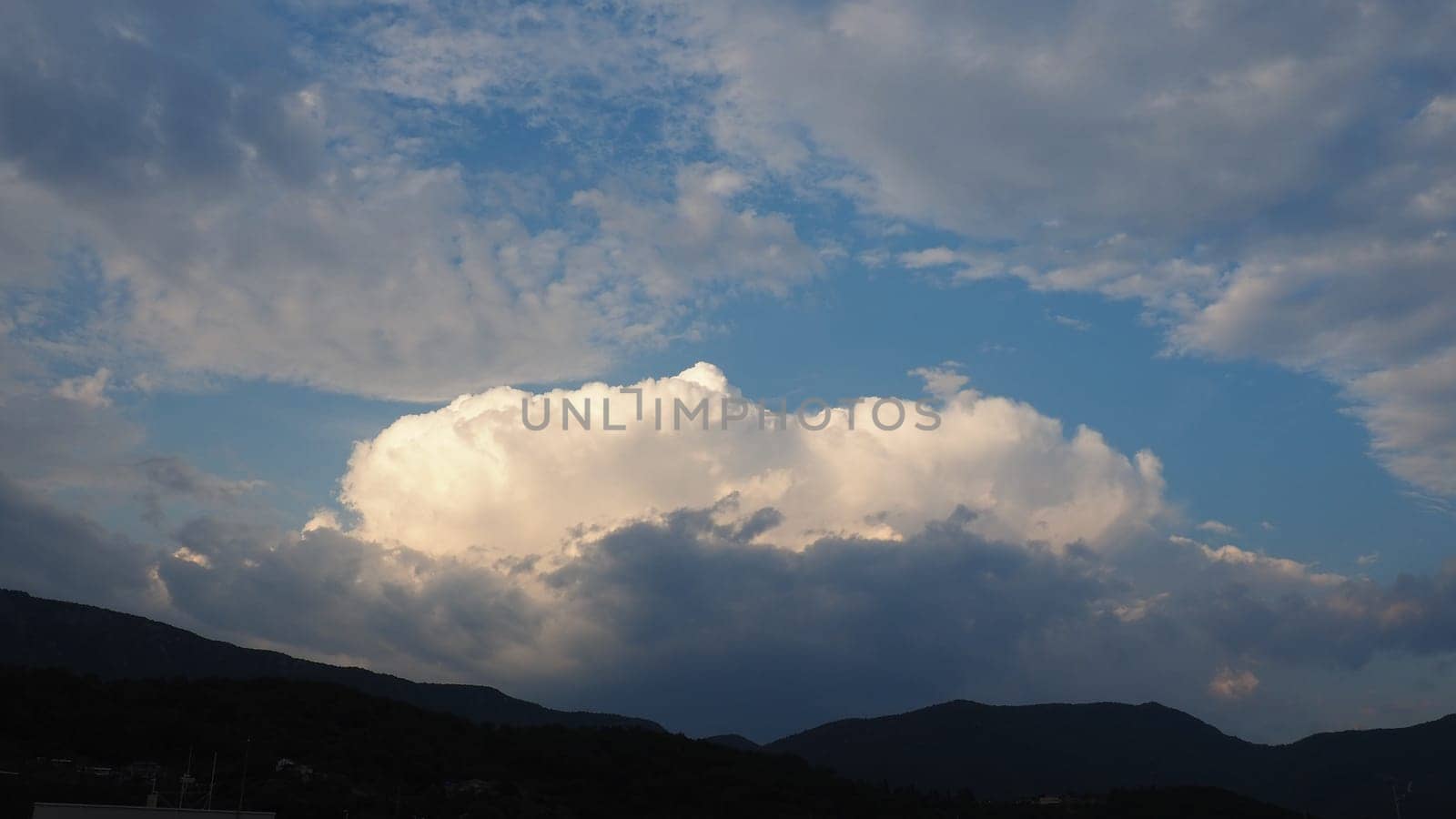 Clouds in the evening sky. The sun's rays pierce the clouds. Blue, yellow and gray colors of the sky and clouds. Beautiful landscape. The sun goes down. Storm weather forecast. Cumulus clouds.