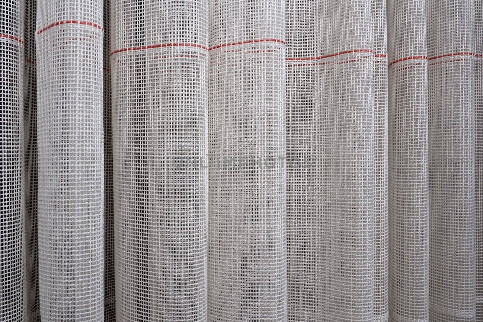 White coarse cotton or linen curtains made of weaves of thin threads. Simple compact economical apartment interior. Window decoration in the room. Red stripe