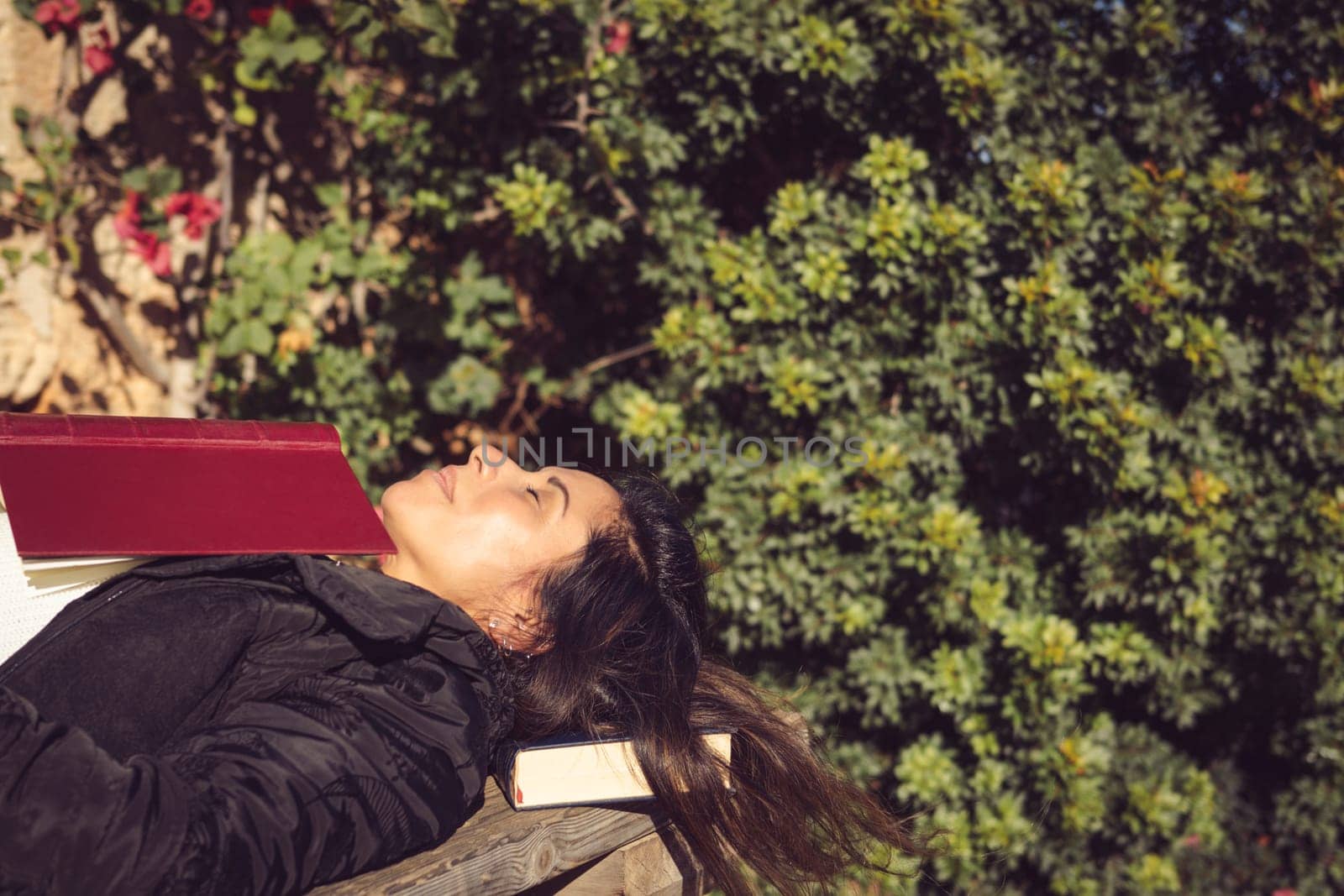woman lying on a wooden table asleep with a book on her chest in the garden of the house.