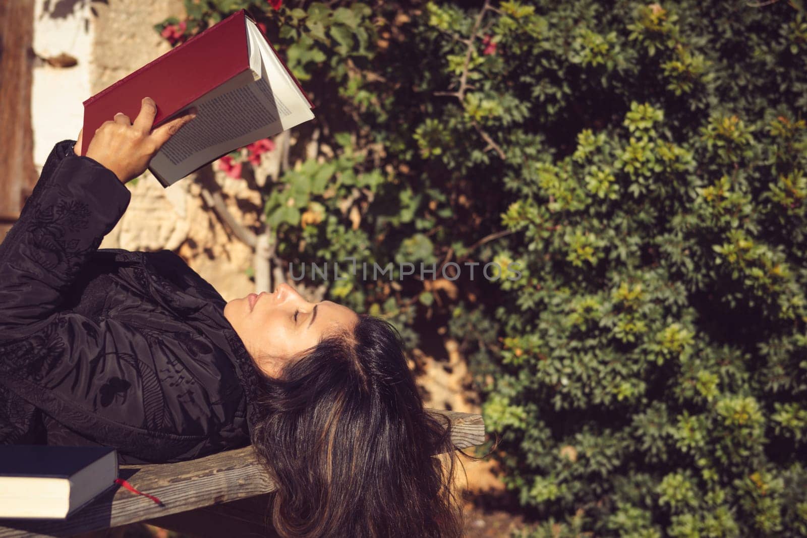 woman holds an open book in the garden, concentrating on reading attentively.