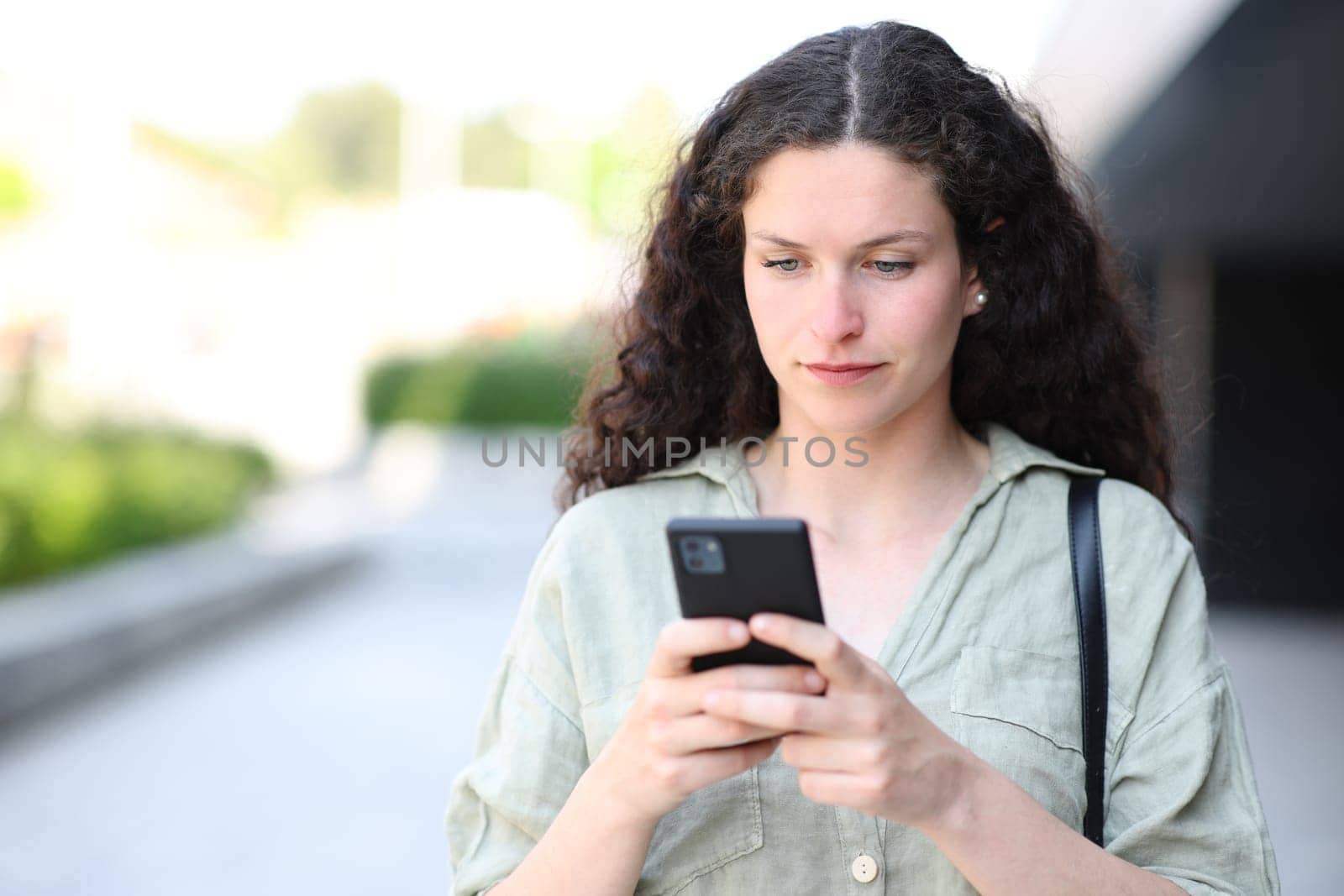 Front view portrait of a woman using phone and walking in the street
