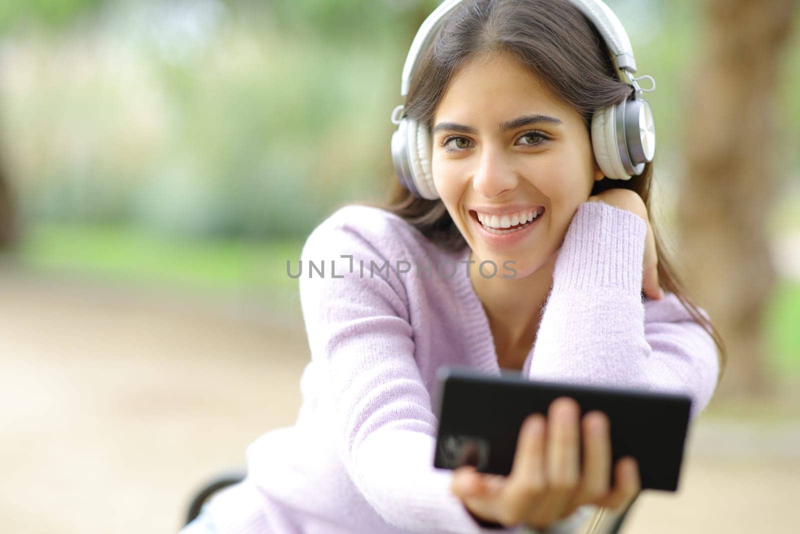 Happy woman looks at you listening to music in a park