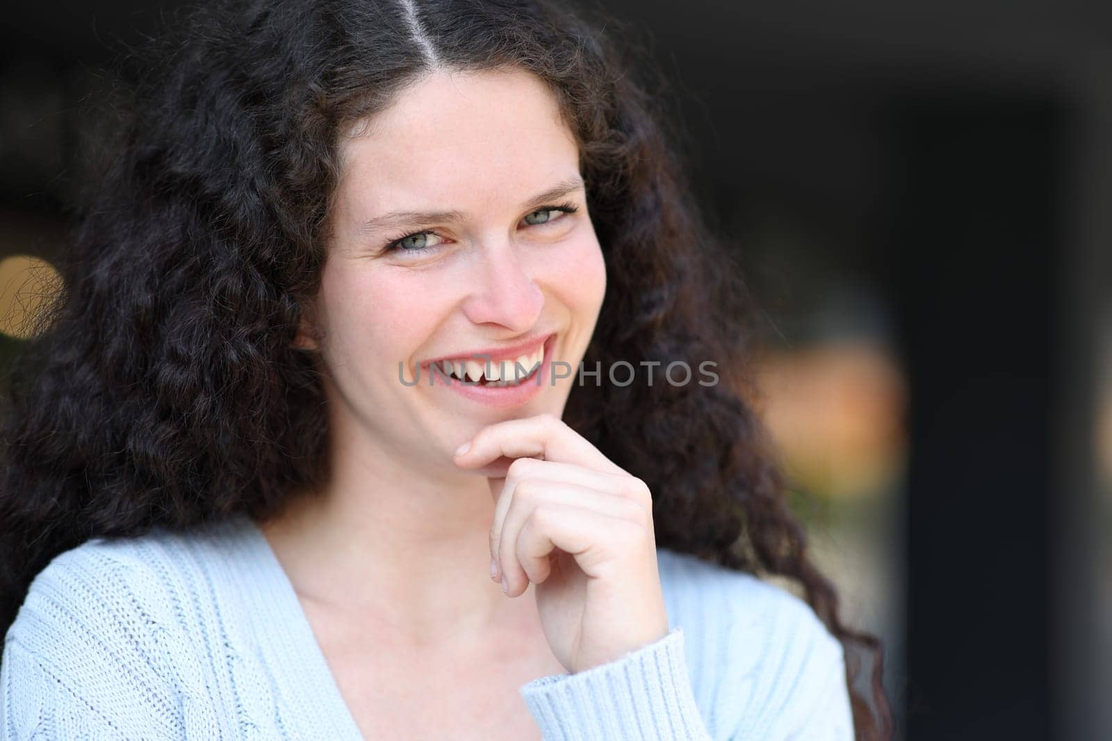 Happy woman smiling with curly hair looking at you in the street