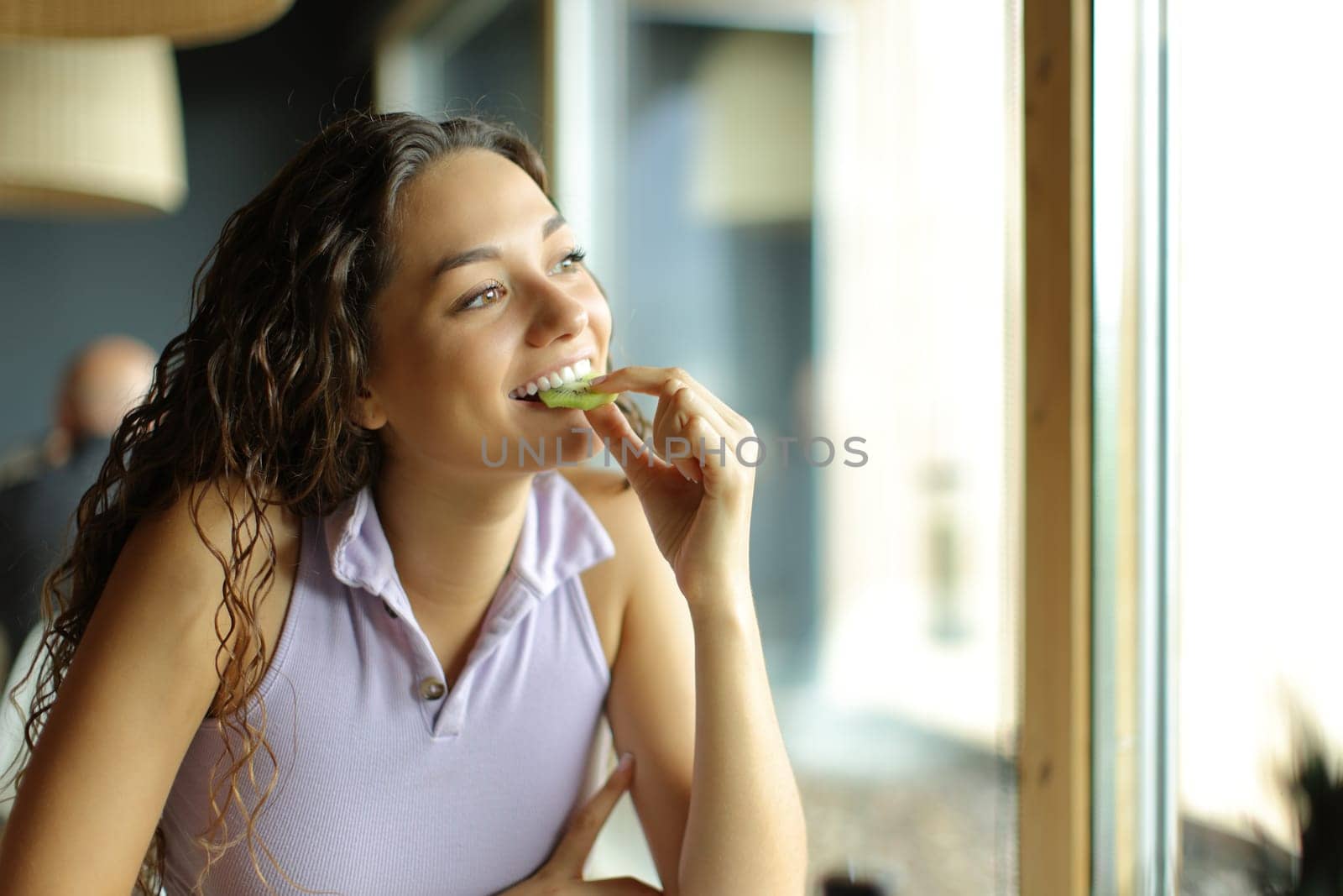 Woman eating kiwi in a restaurant looking through a window