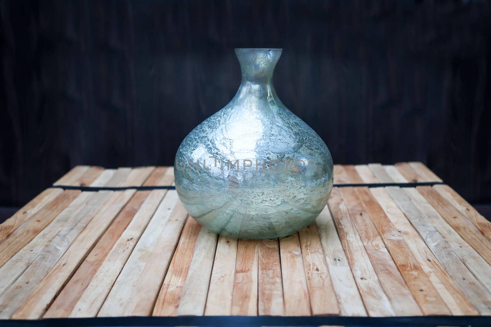 A still life with a blue vase on a stack of wooden slats, against a dark background.