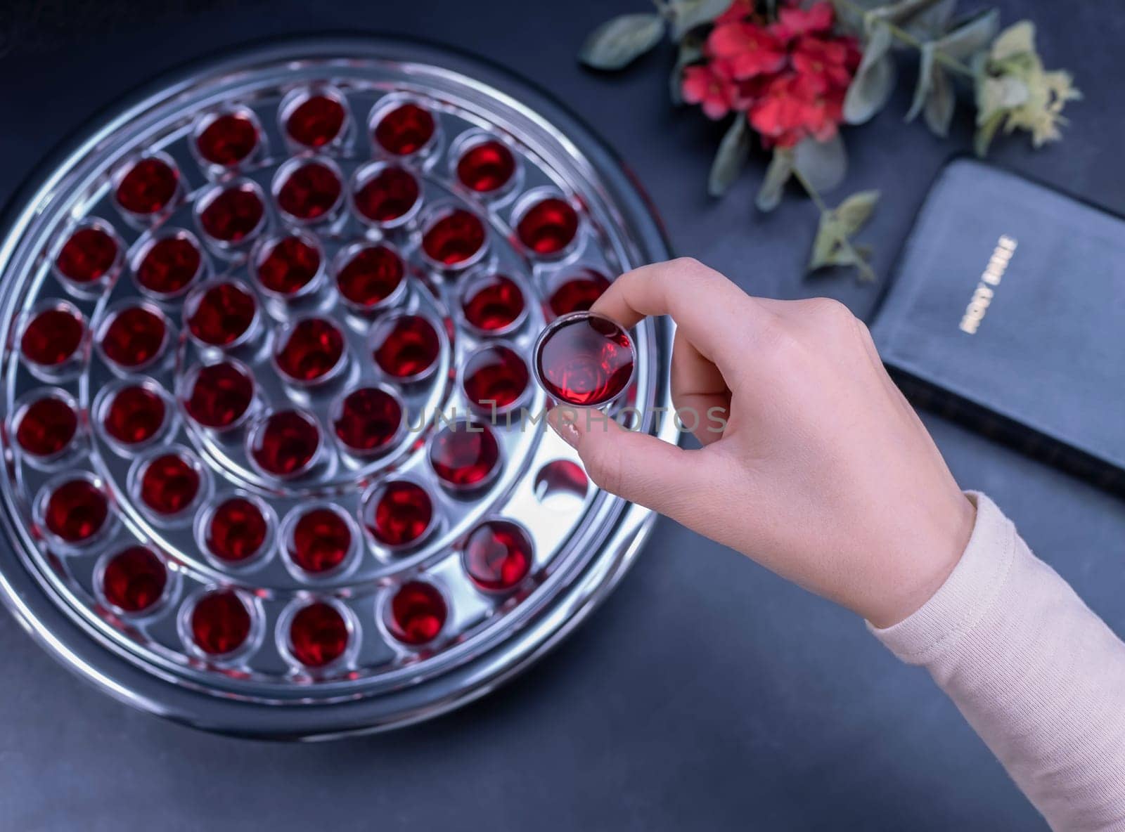 Closeup of young woman taking communion the wine symbol of Jesus Christ blood in small cups on black background. Easter Passover and Lord Supper concept.