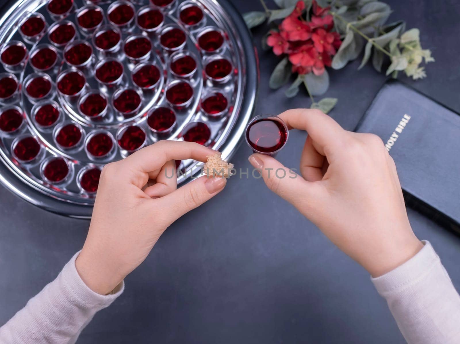 Closeup of young woman taking communion the wine symbol of Jesus Christ blood in small cups on black background. Easter Passover and Lord Supper concept.
