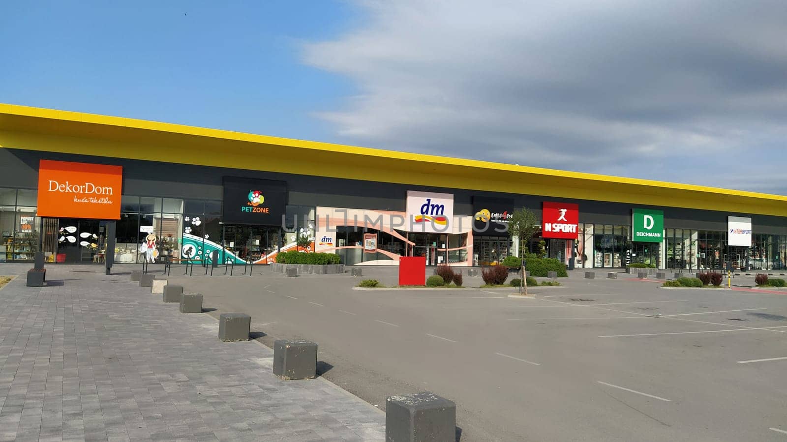 Stop shop shopping center, Sremska Mitrovica, Serbia, June 06, 2022. Square with open shops dm, intersport, dekordom, ccc, lc waikiki. People, parking and pavement. Sunny summer day.