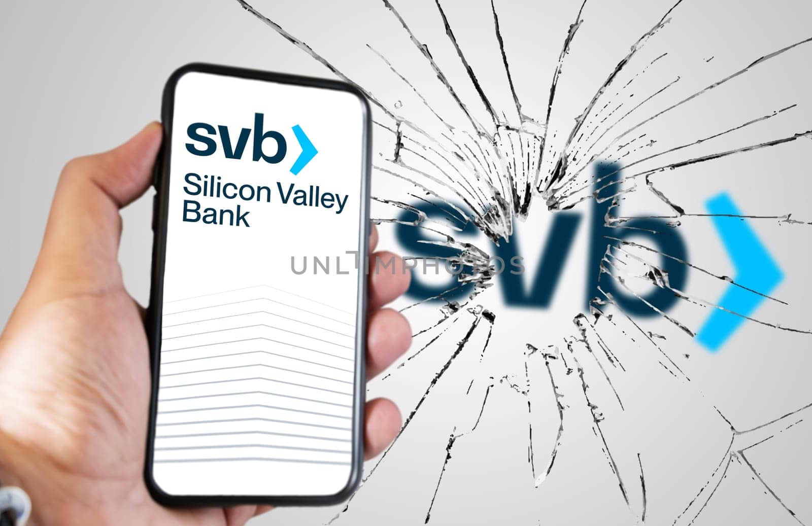 Santa Clara, USA, March 2023: Hand holding a phone with Silicone Valley Bank website on the screen with broken glass and blurred SVB logo in the background. Bank run and bankruptcy.