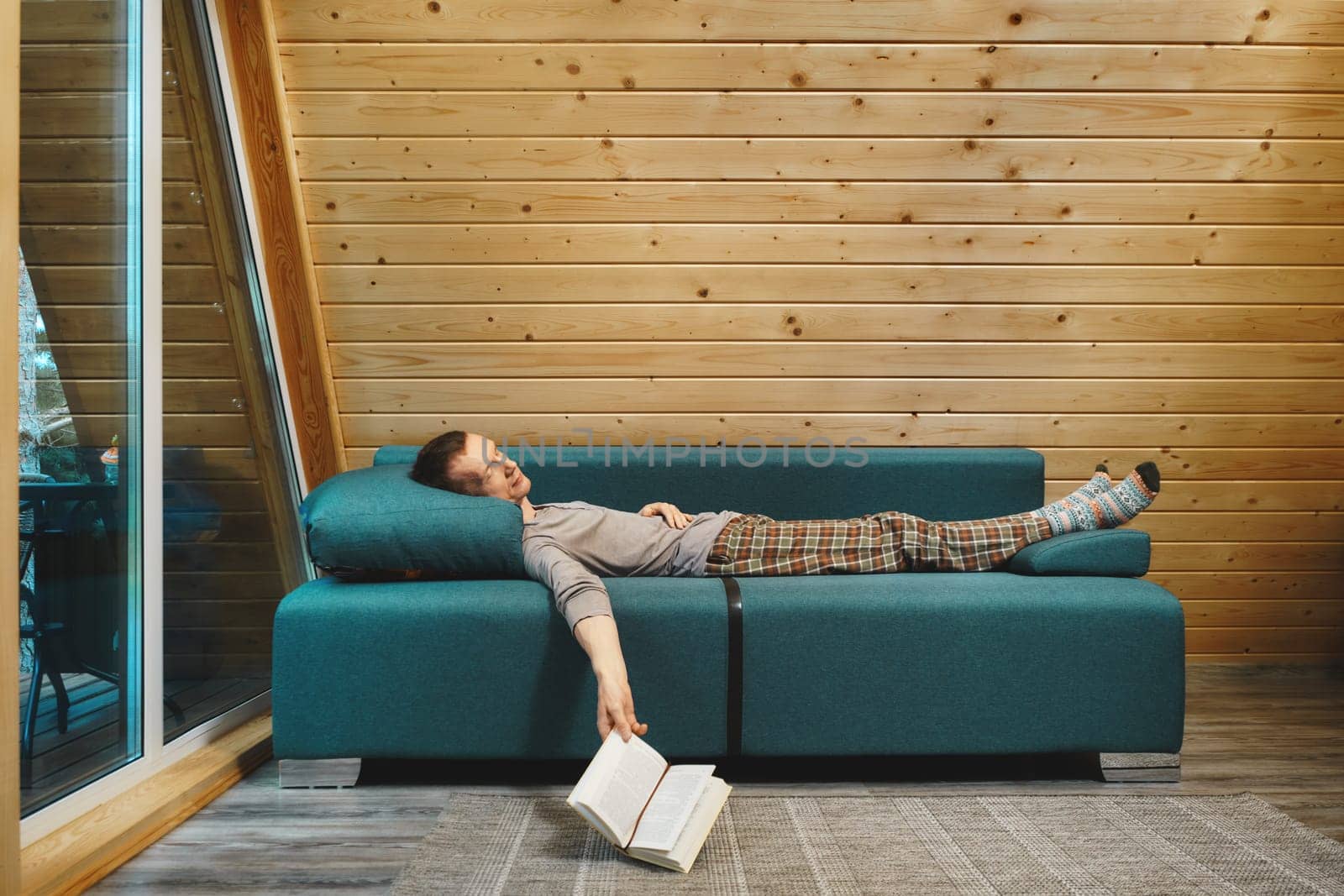 Man was reading a book in his wooden cabin in rainy day and fell asleep