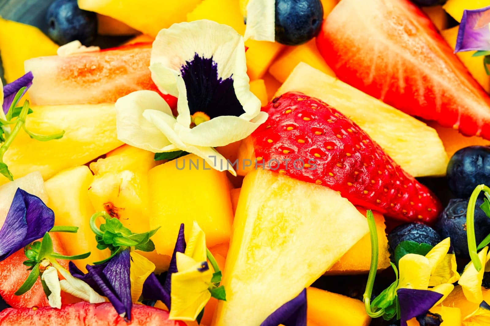 Salad of pineapple, strawberries and berries, decorated with edible flowers.