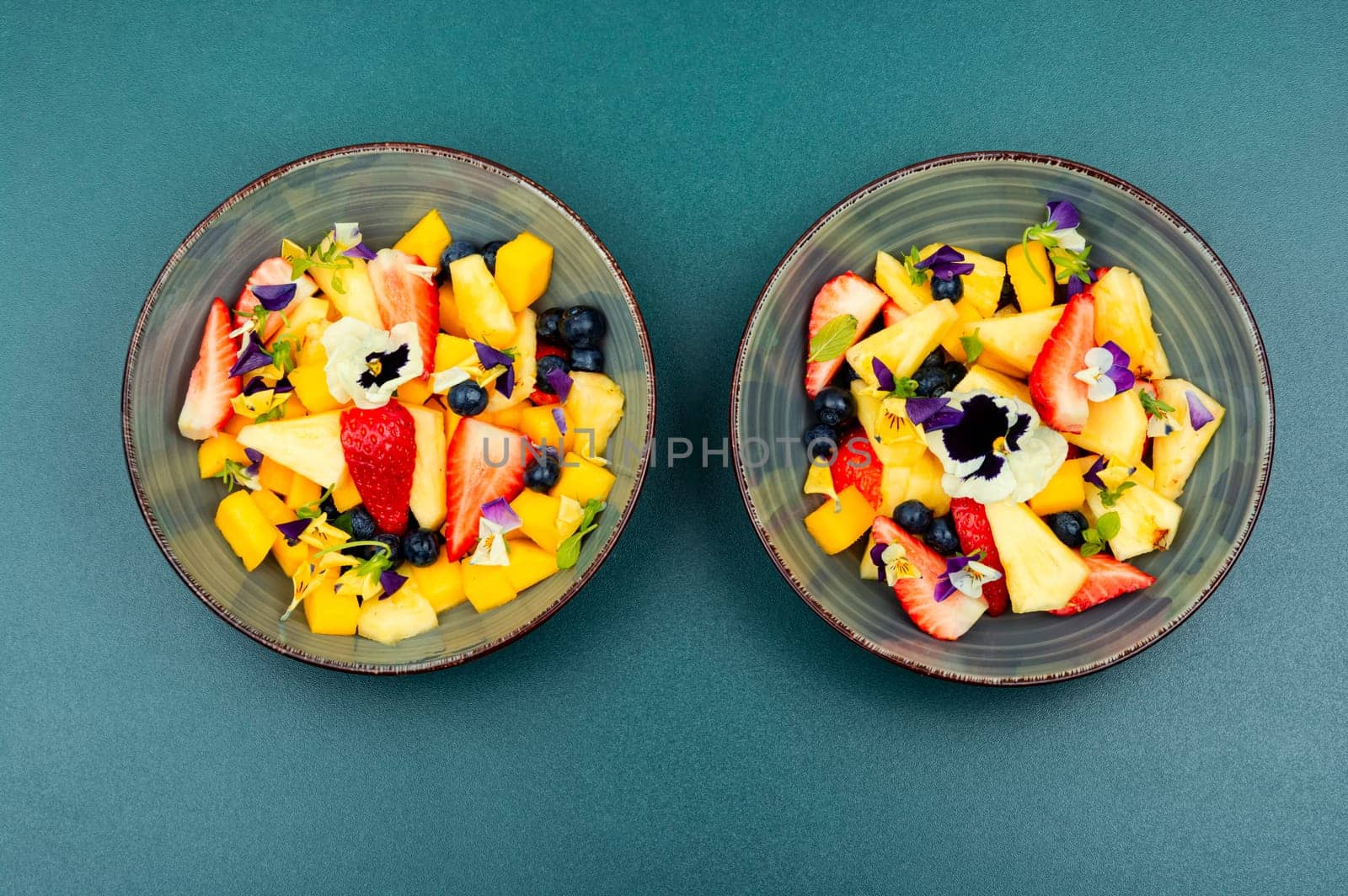 Salad of pineapple, strawberries and berries, decorated with edible flowers.