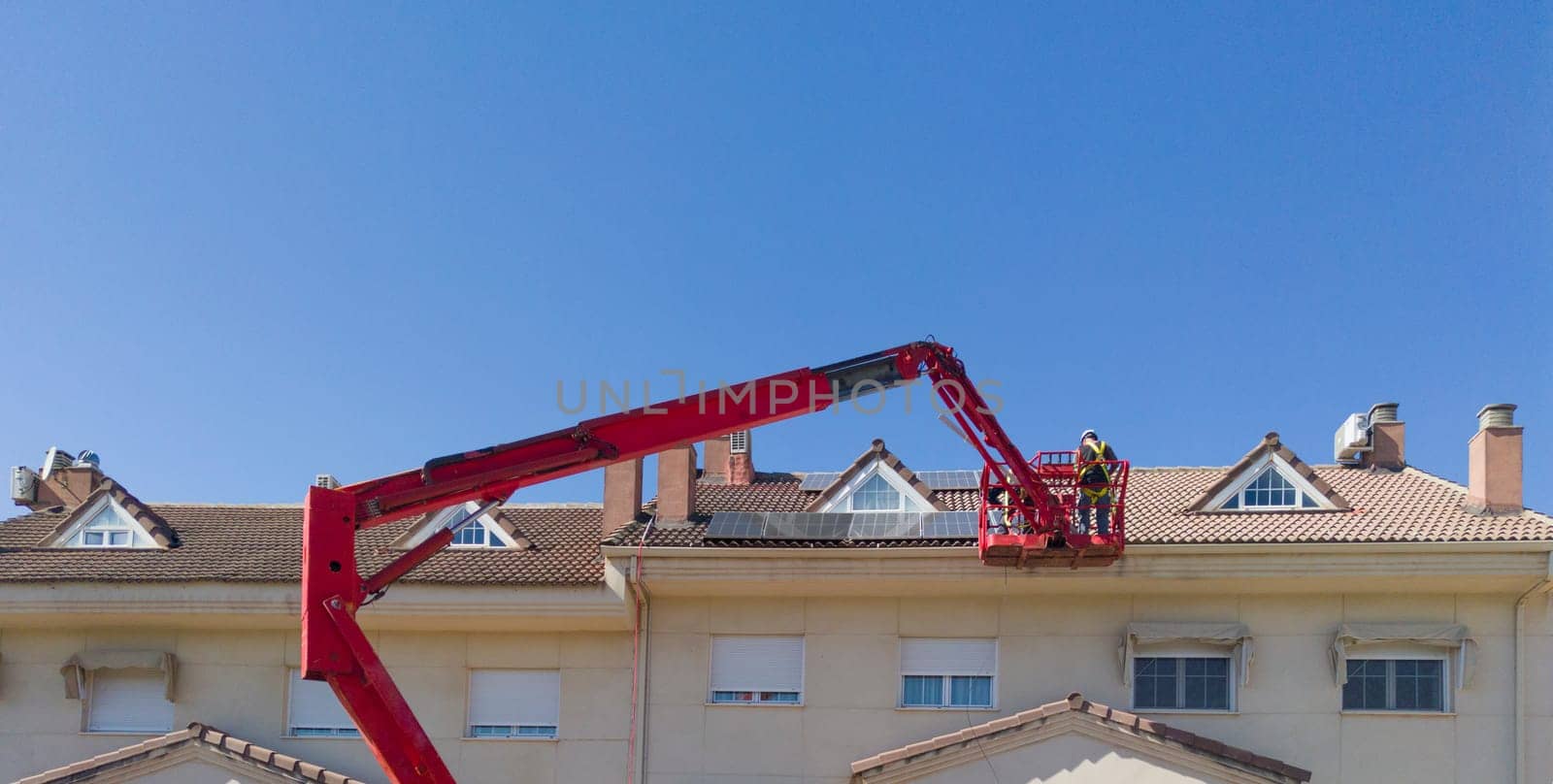 Workmen installing solar panels on the roof of a terraced house. They working over articulated boom lift
