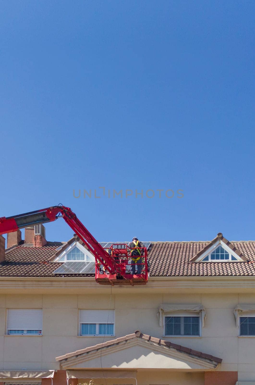 Workmen installing solar panels on the roof of a terraced house. They working over articulated boom lift