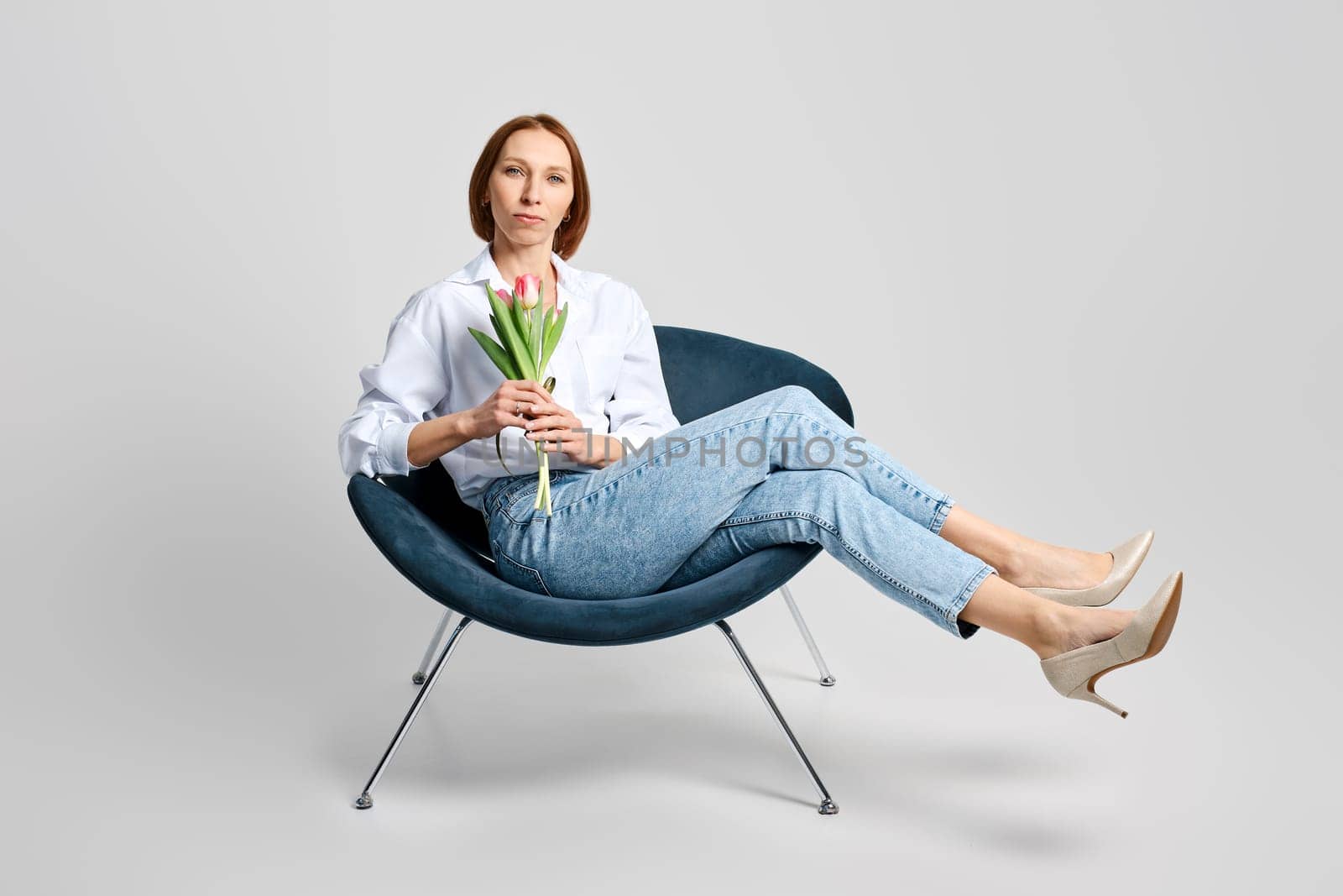 Studio portrait of cheerful meddle aged woman in armchair with tulips in hand