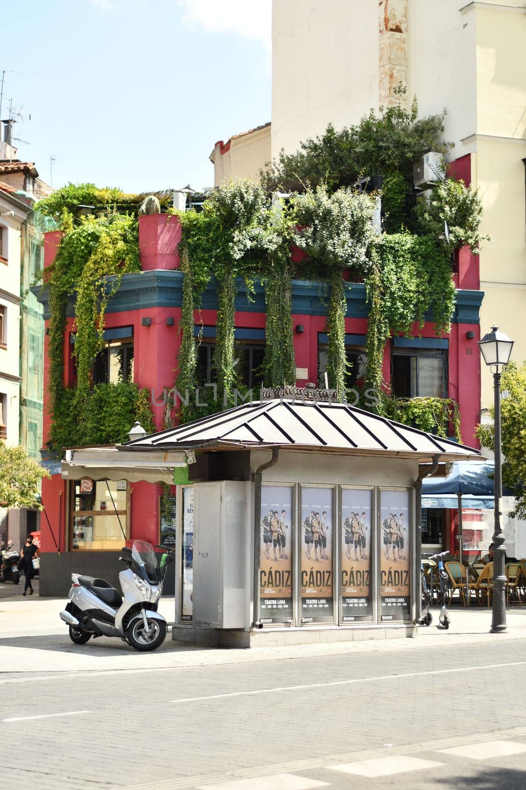Vertical shot of a kiosk and scooter in front of a building overgrown with vegetation