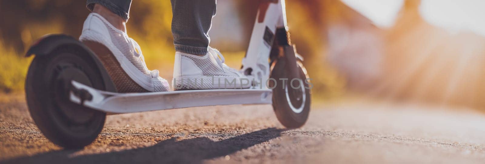 Woman riding on scooter on asphalt road in summer. Close-up view. Concept of city life.