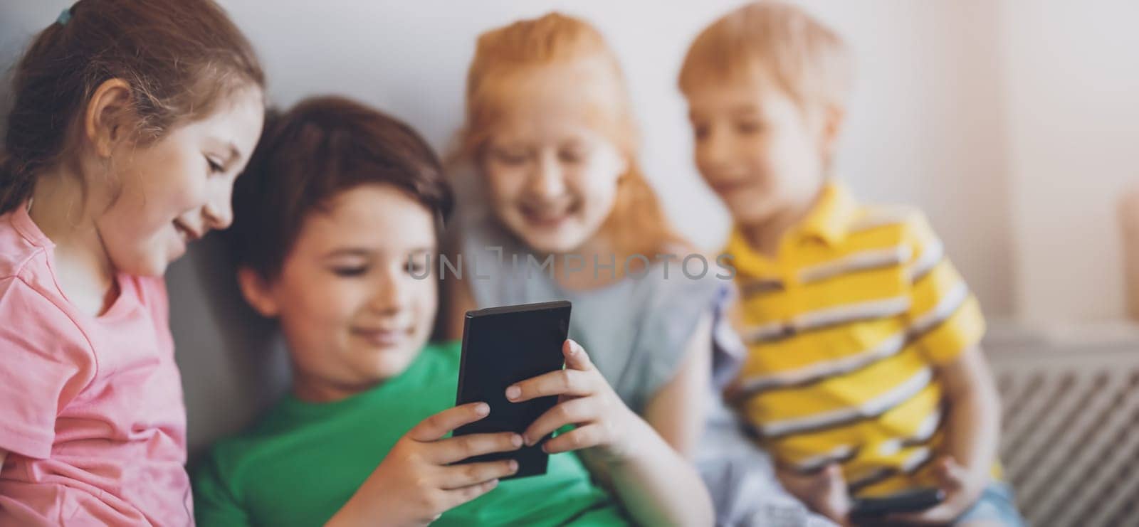Group of children sitting indoors and looking in the smartphone. Concept of relationship, friendship and using of smart technologies.