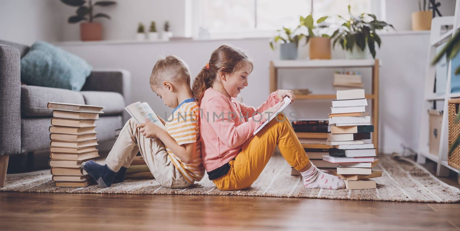 Two children sitting on the floor in the room and reading books. Concept of the family relationship, education and hobby.