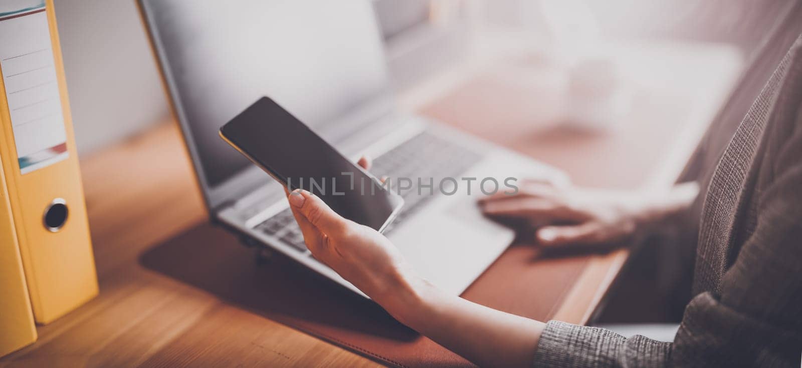 Woman with smartphone in her hand working on the laptop in office. Place of work. Close-up view.