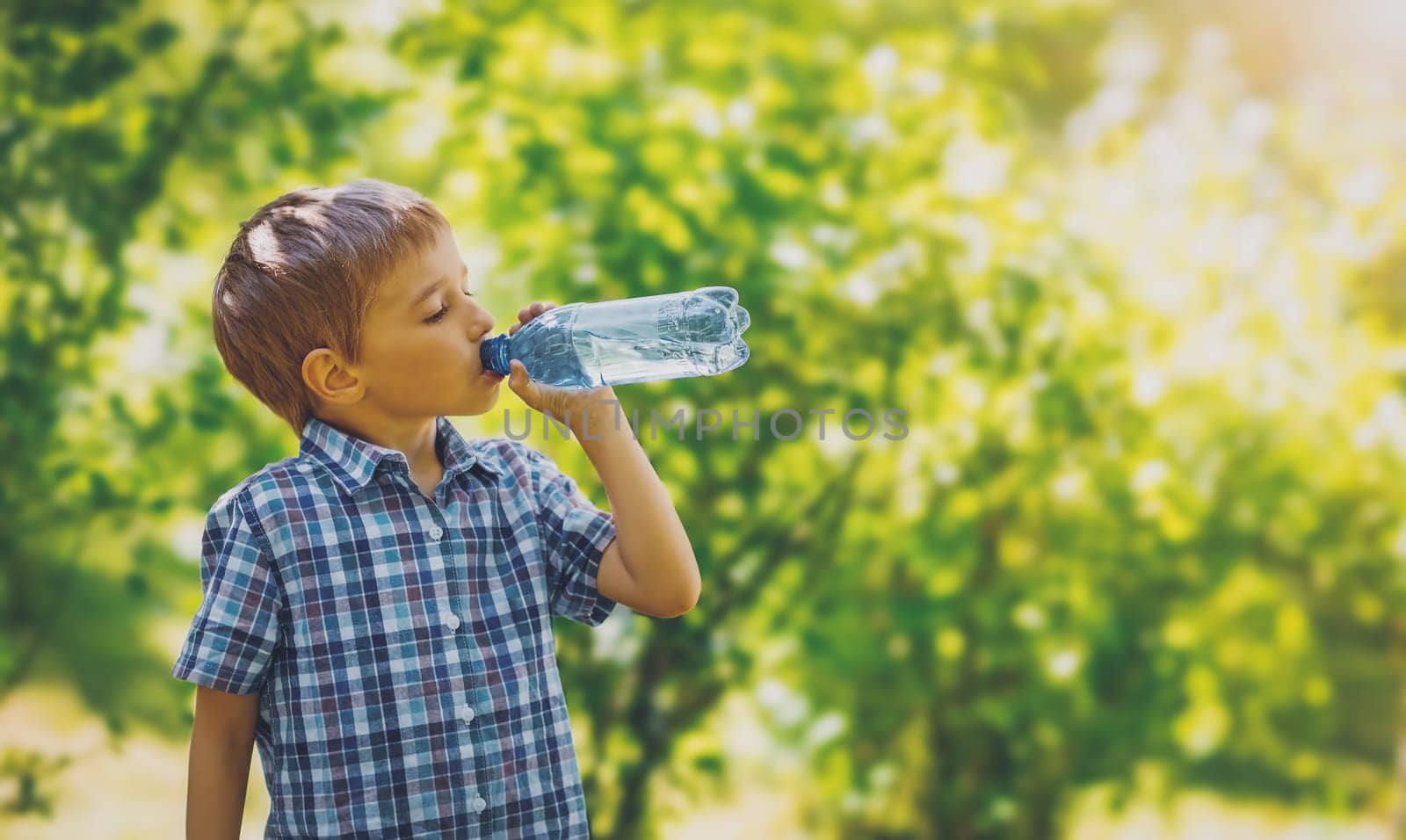Cute boy drinking a bottle of pure water in nature. Concept of the provision of clean, mineral aqua in the world.