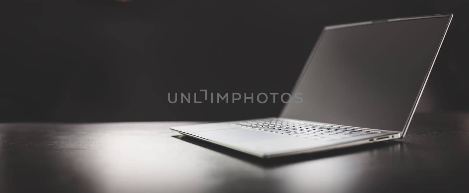 Grey laptop on the dark table on the black background. Concept of the backdrop and banner.