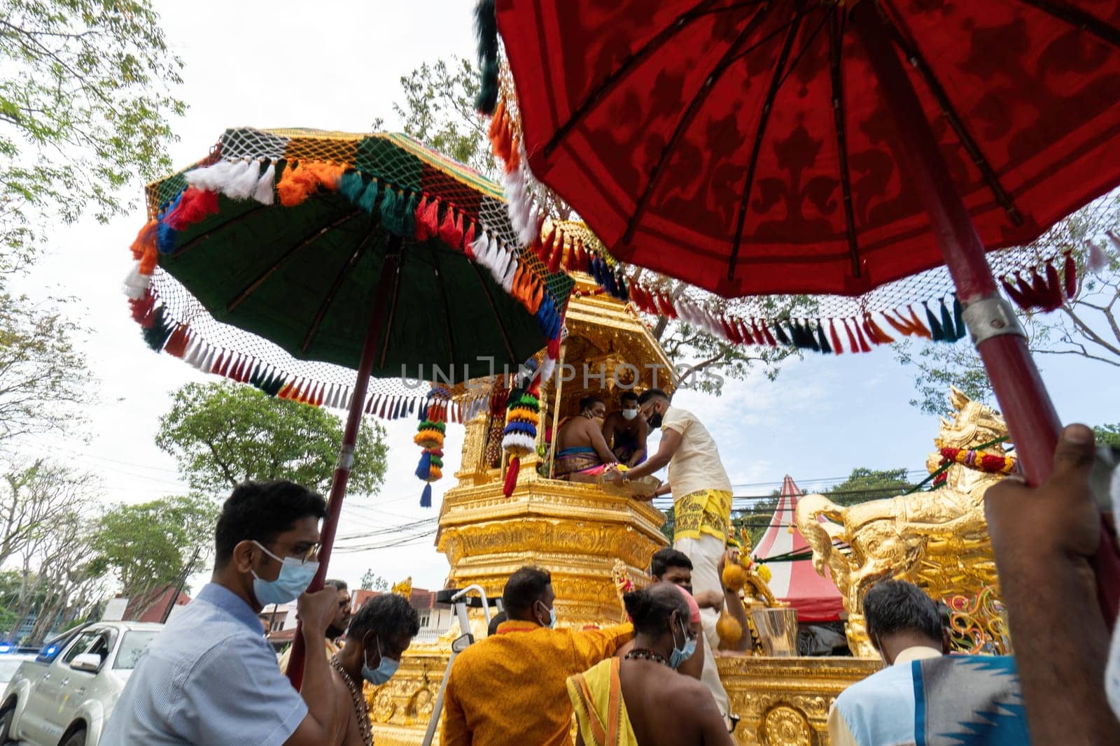 George Town, Penang, Malaysia - Jan 17 2022: Hindu volunteer wear mask carry umbrella near gold chariot