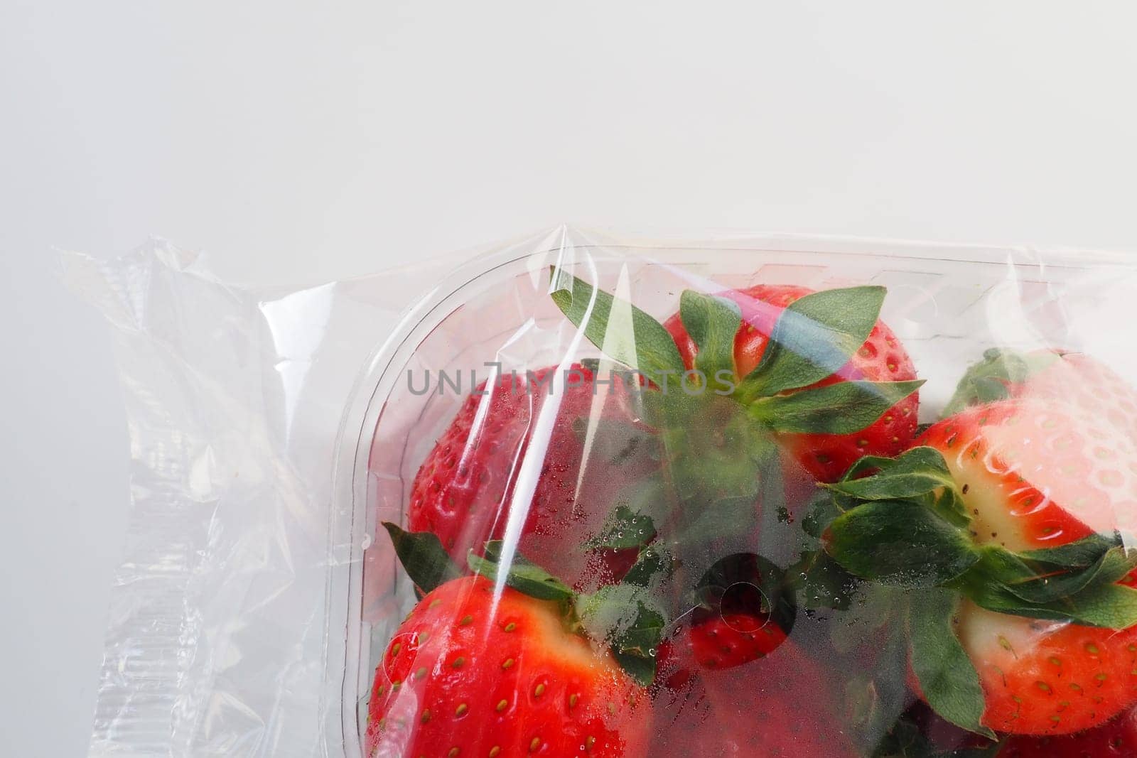 Ripe strawberries in a plastic package on a white background. Delicious fresh berries in a container for sale to customers. Keeping food fresh. Healthy food, vitamins and microelements