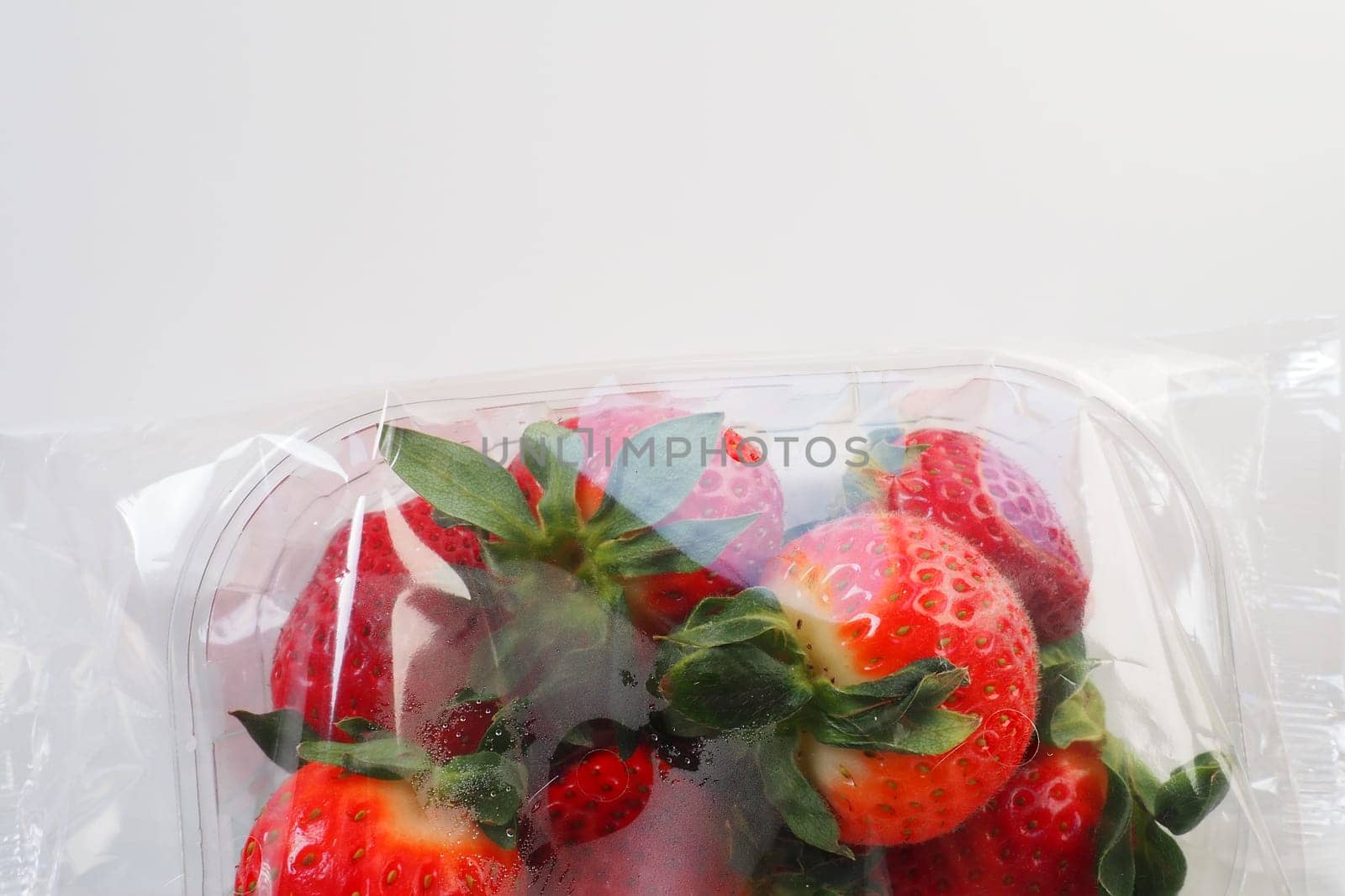 Ripe strawberries in a plastic package on a white background. Delicious fresh berries in a container for sale to customers. Keeping food fresh. Healthy food, vitamins and microelements