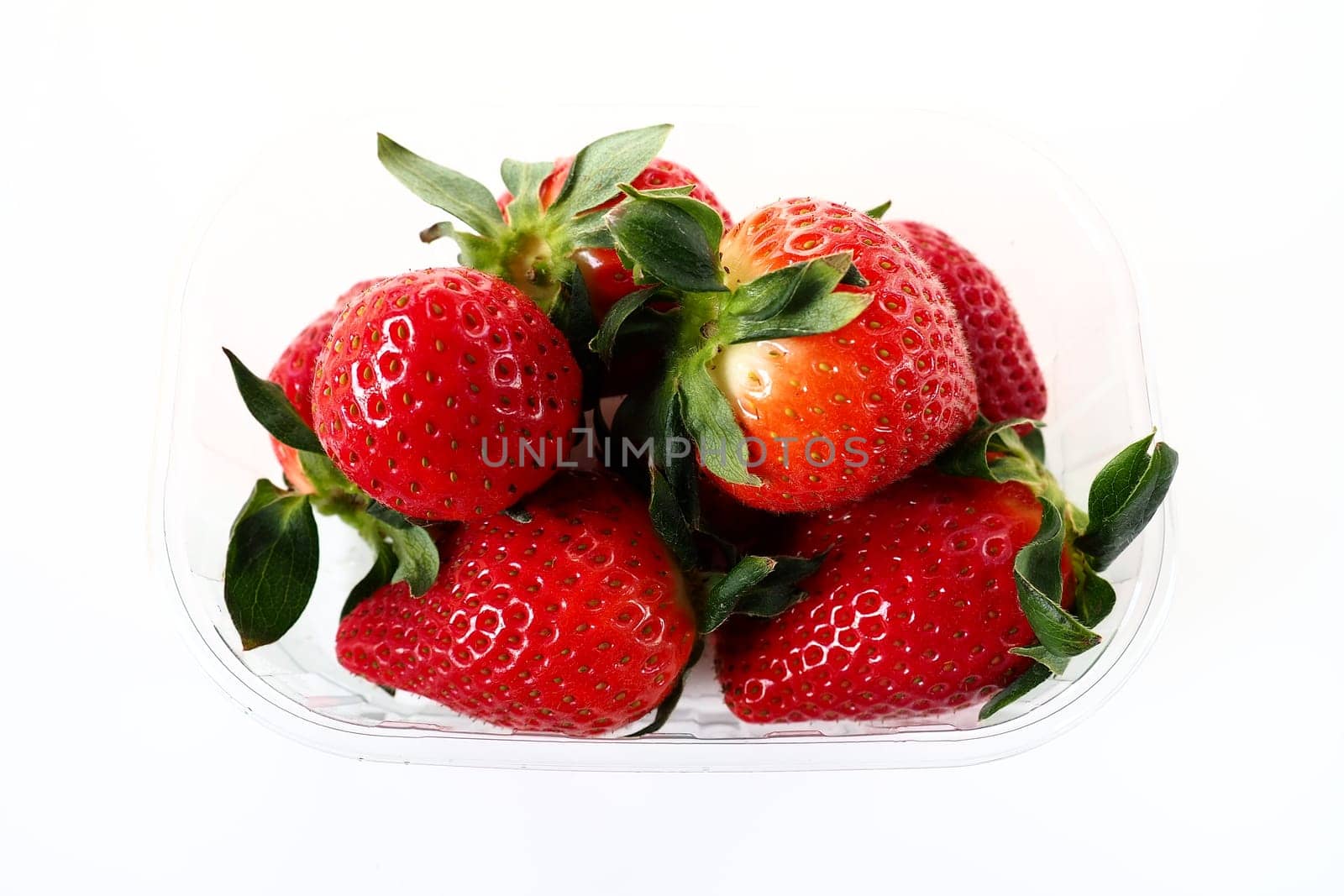 Ripe strawberries in a plastic package on a white background. Delicious fresh berries in a container for sale to customers. Keeping food fresh. Healthy food, vitamins and microelements