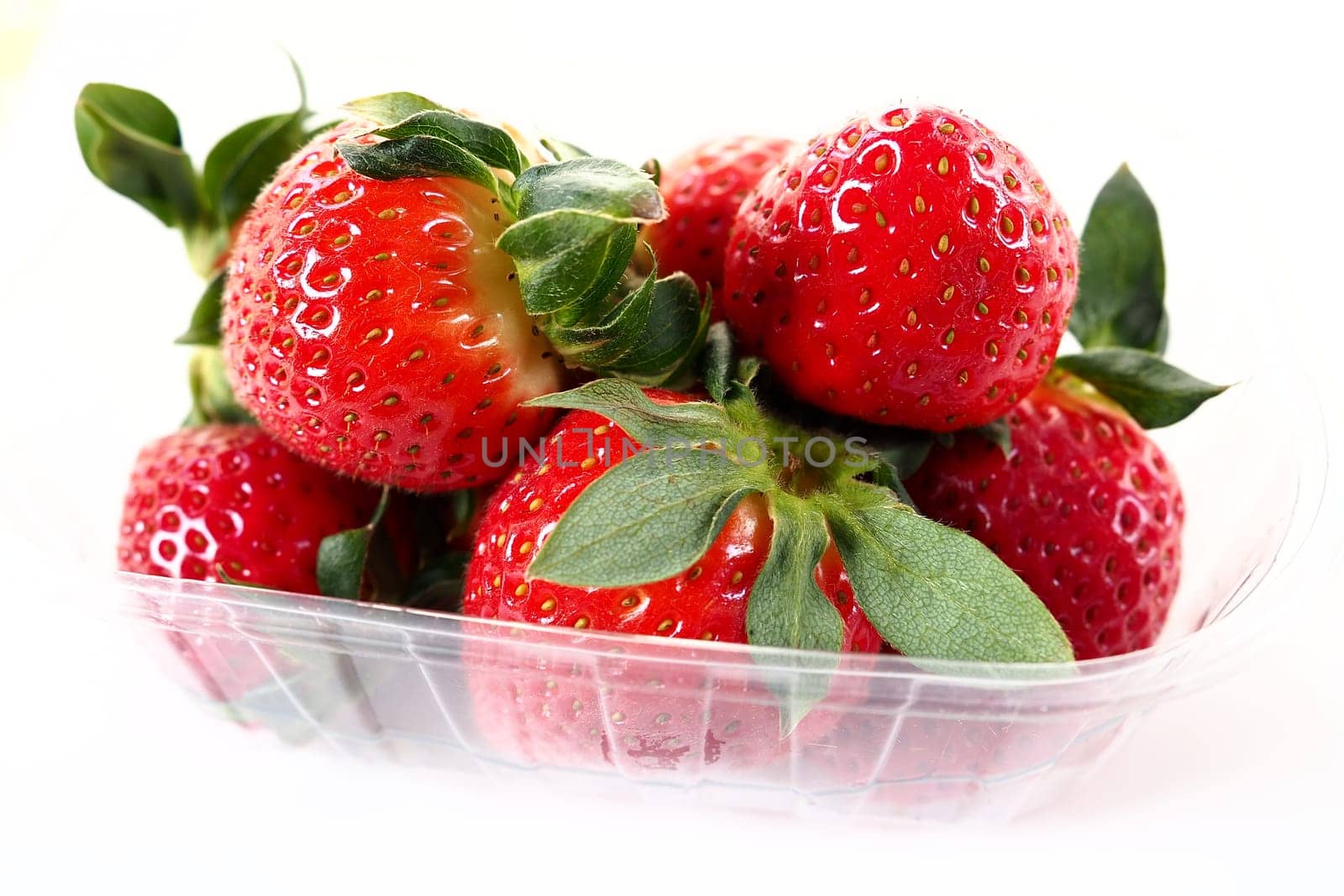 Ripe strawberries in a plastic package on a white background. Delicious fresh berries in a container for sale to customers. Keeping food fresh. Healthy food, vitamins and microelements